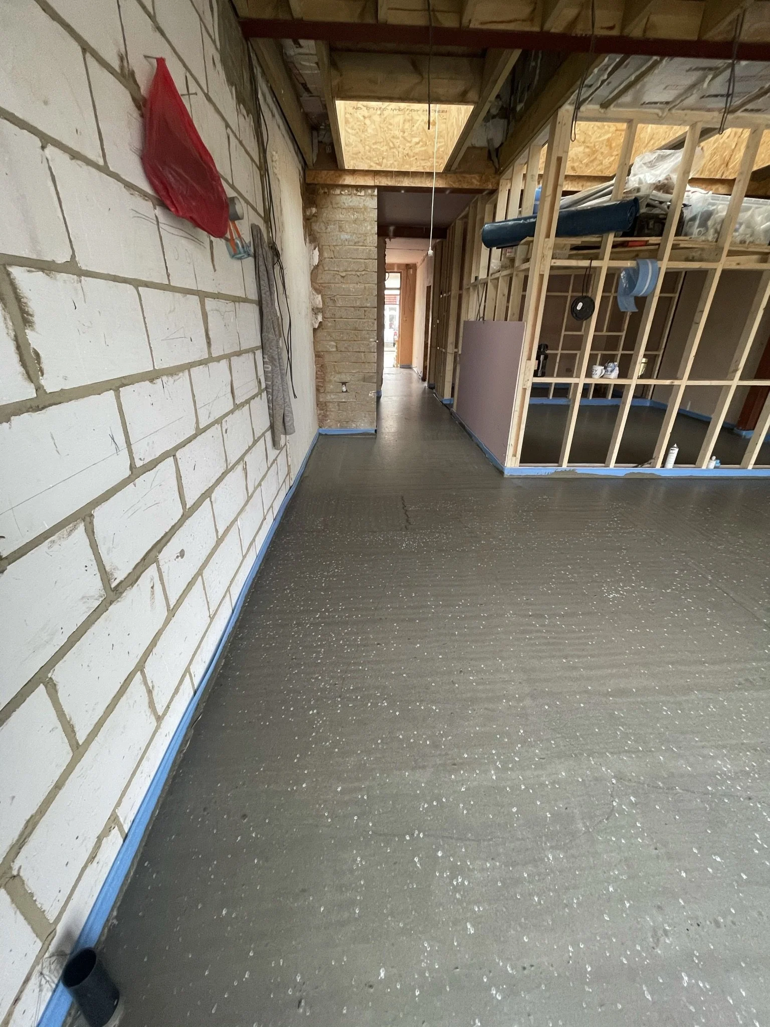 Partially renovated interior with exposed wall framing, unfinished ceiling, brick partition, electrical wiring, construction materials, and a dark concrete floor.