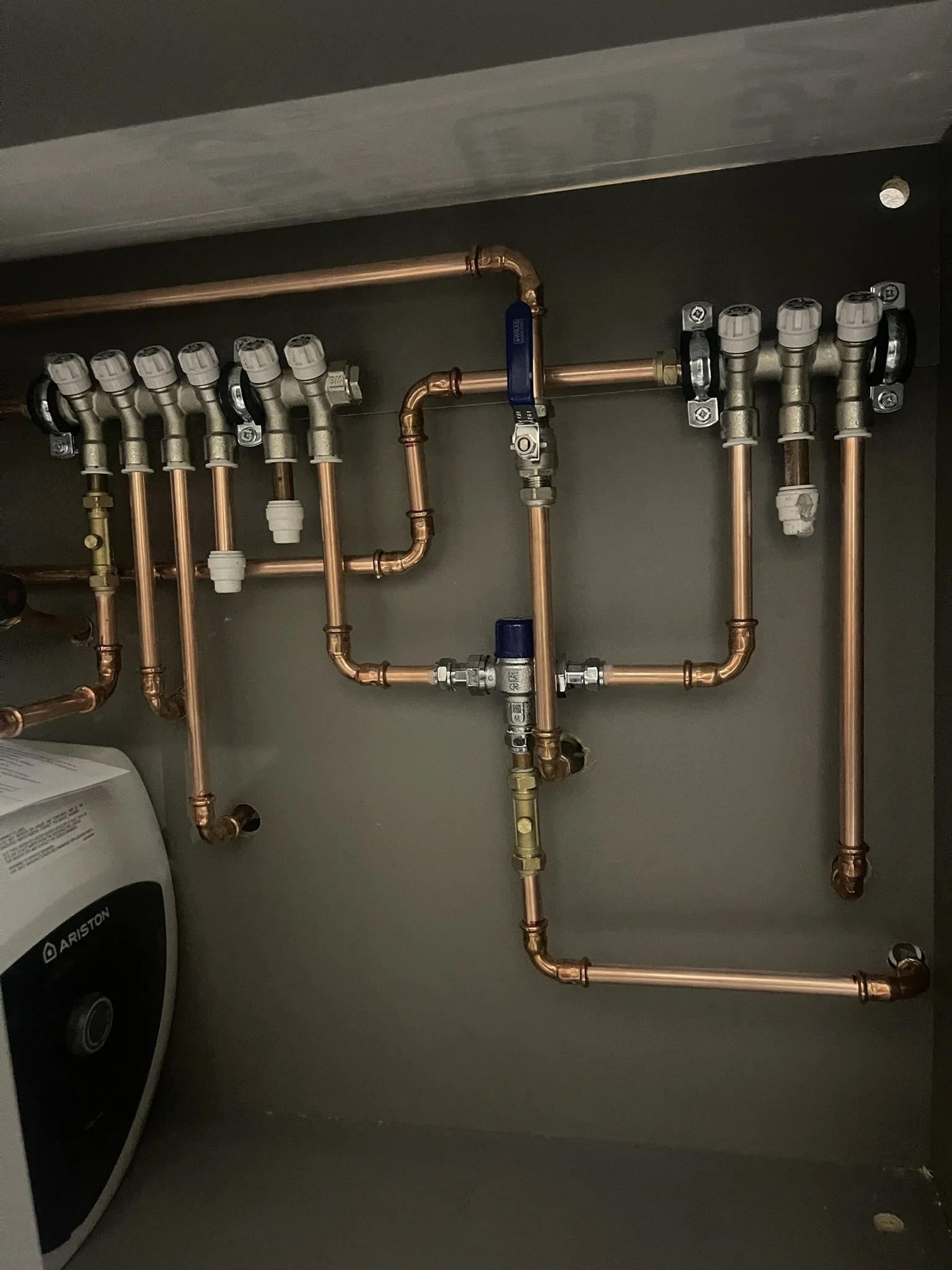 Copper plumbing manifold with multiple valves, water pipes, and an Ariston boiler
