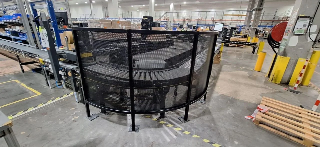 Protection cintrée en tôle perforée noire autour d’un convoyeur dans un entrepôt logistique, réalisée par Austral