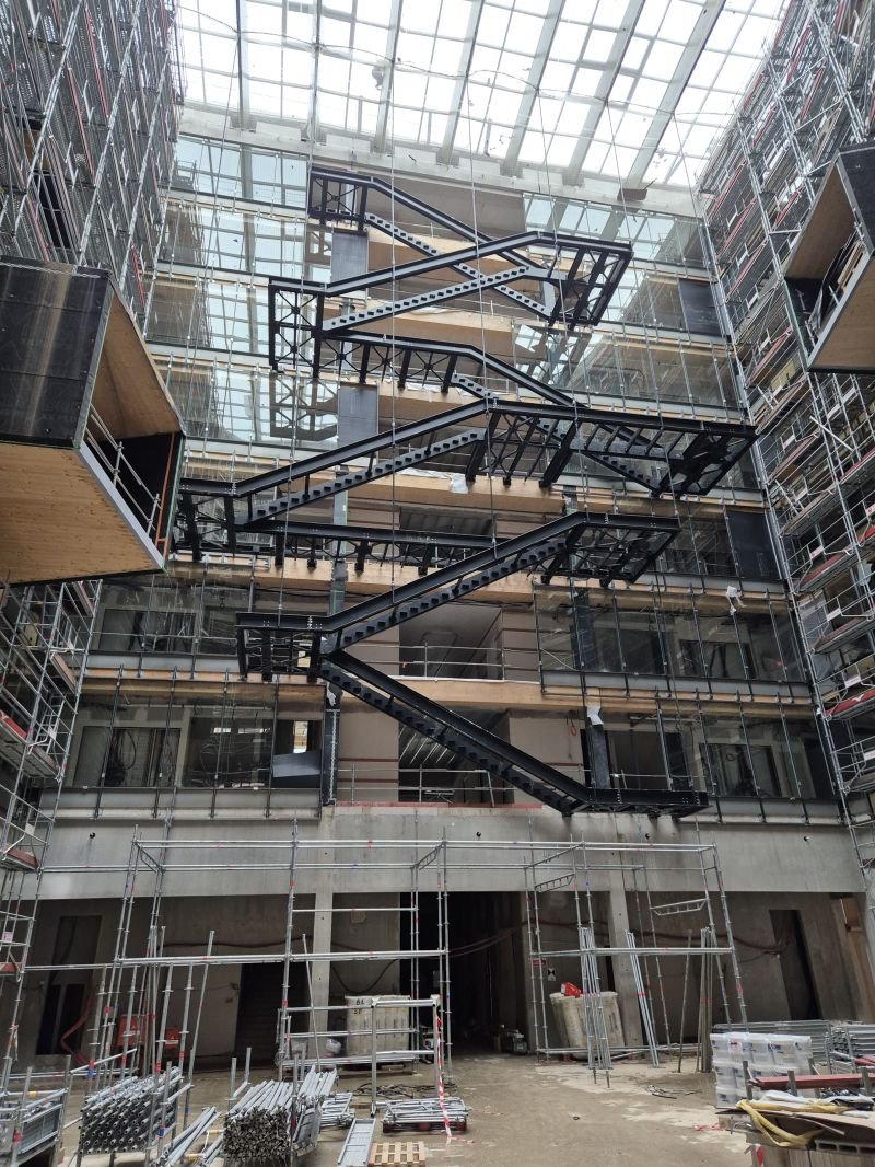 Escalier métallique monumental à volées droites dans un atrium sous verrière, en cours de montage par Austral