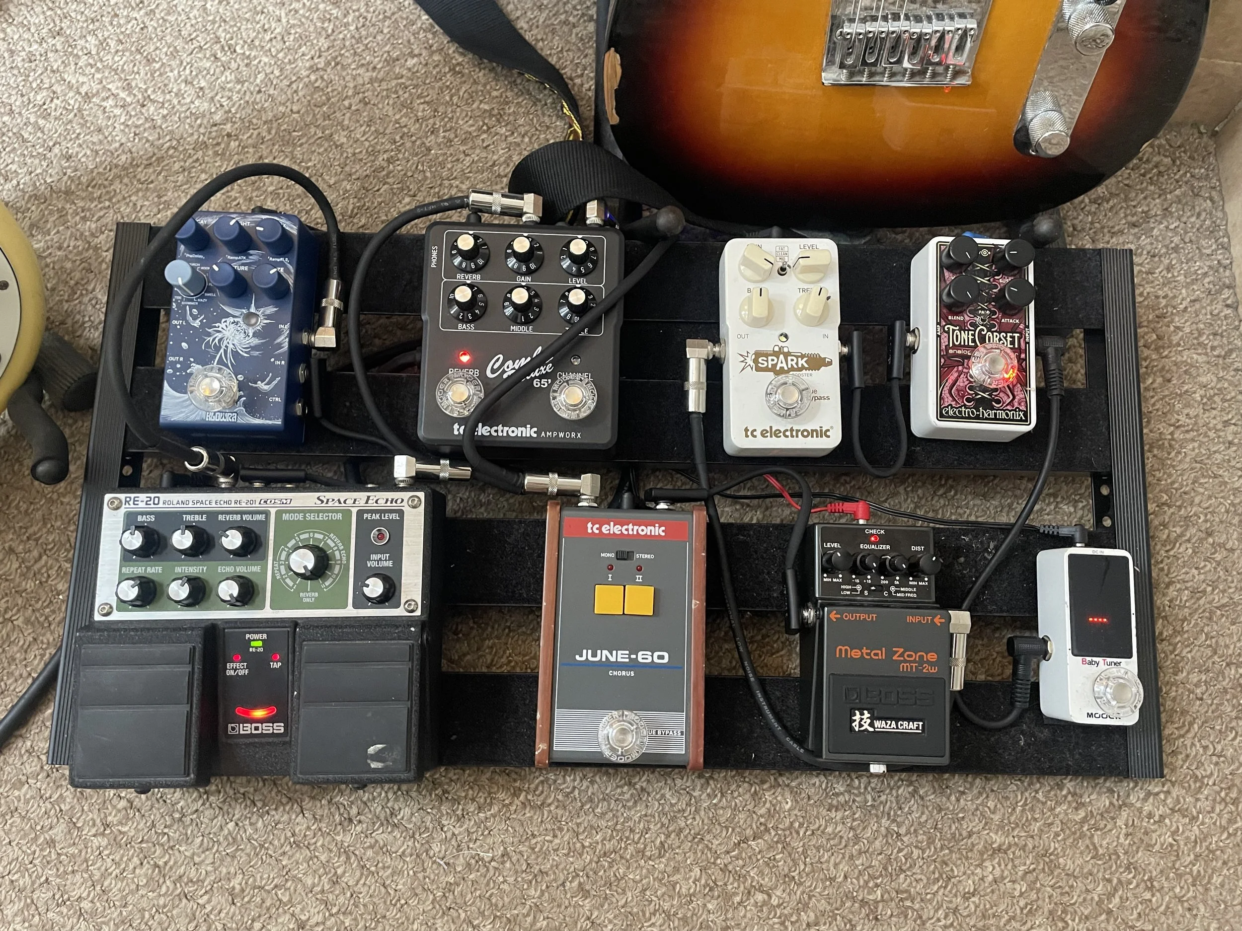 Top view of a guitar effects pedalboard with multiple effects pedals connected by cables, placed on a carpeted floor.