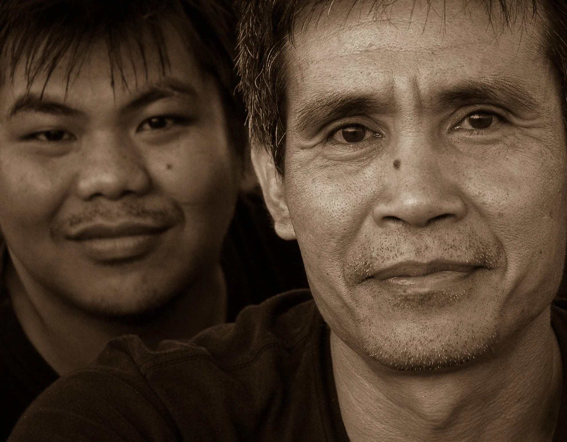 Close-up of two men's faces, one East Asian and one of South Asian or Southeast Asian descent, posing indoors.