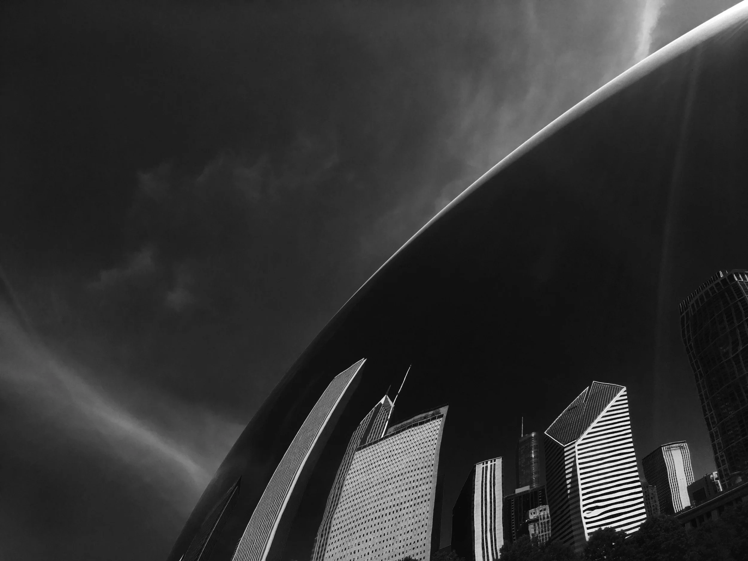 Black and white photo of modern skyscrapers viewed from below against a dark cloudy sky.