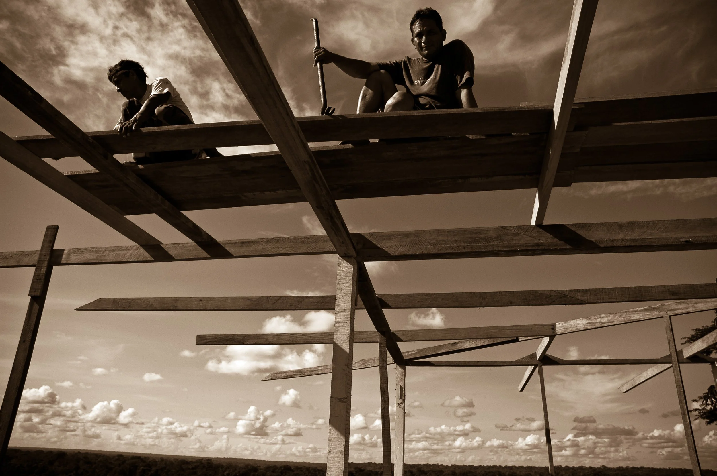 Two children building a wooden structure outdoors against a sky with clouds.
