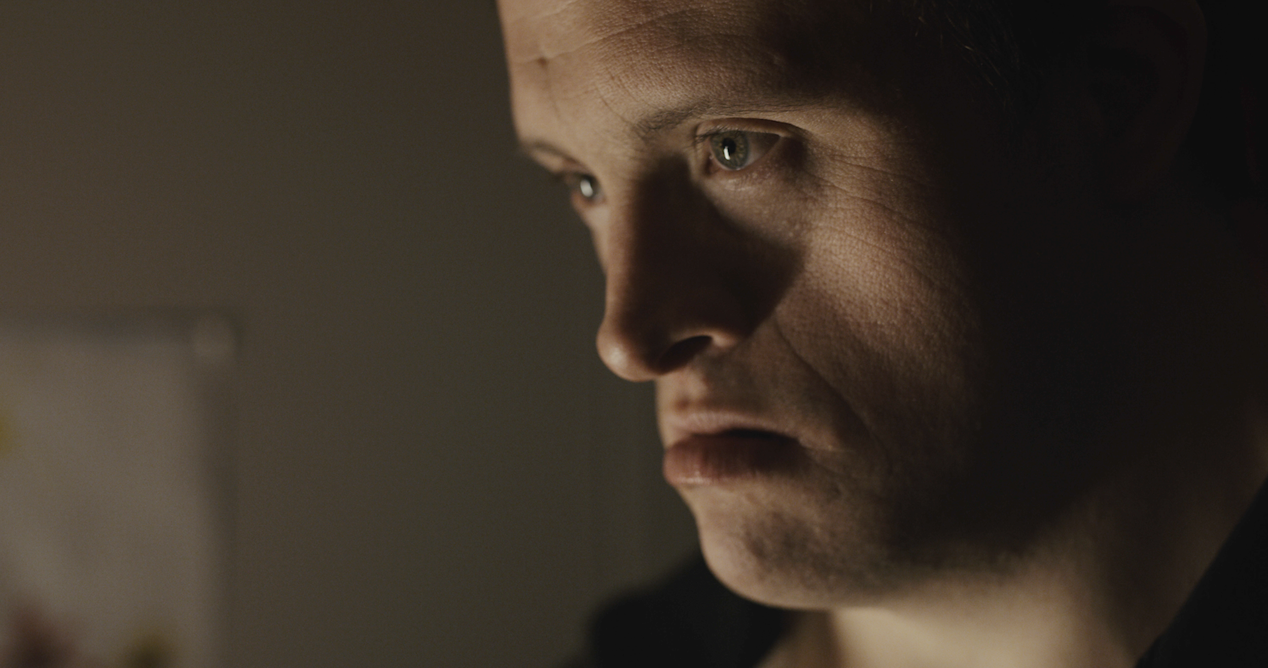 Close-up of a person's face showing a serious expression, with a focus on the person's left eye and part of their nose and lips, in low lighting.
