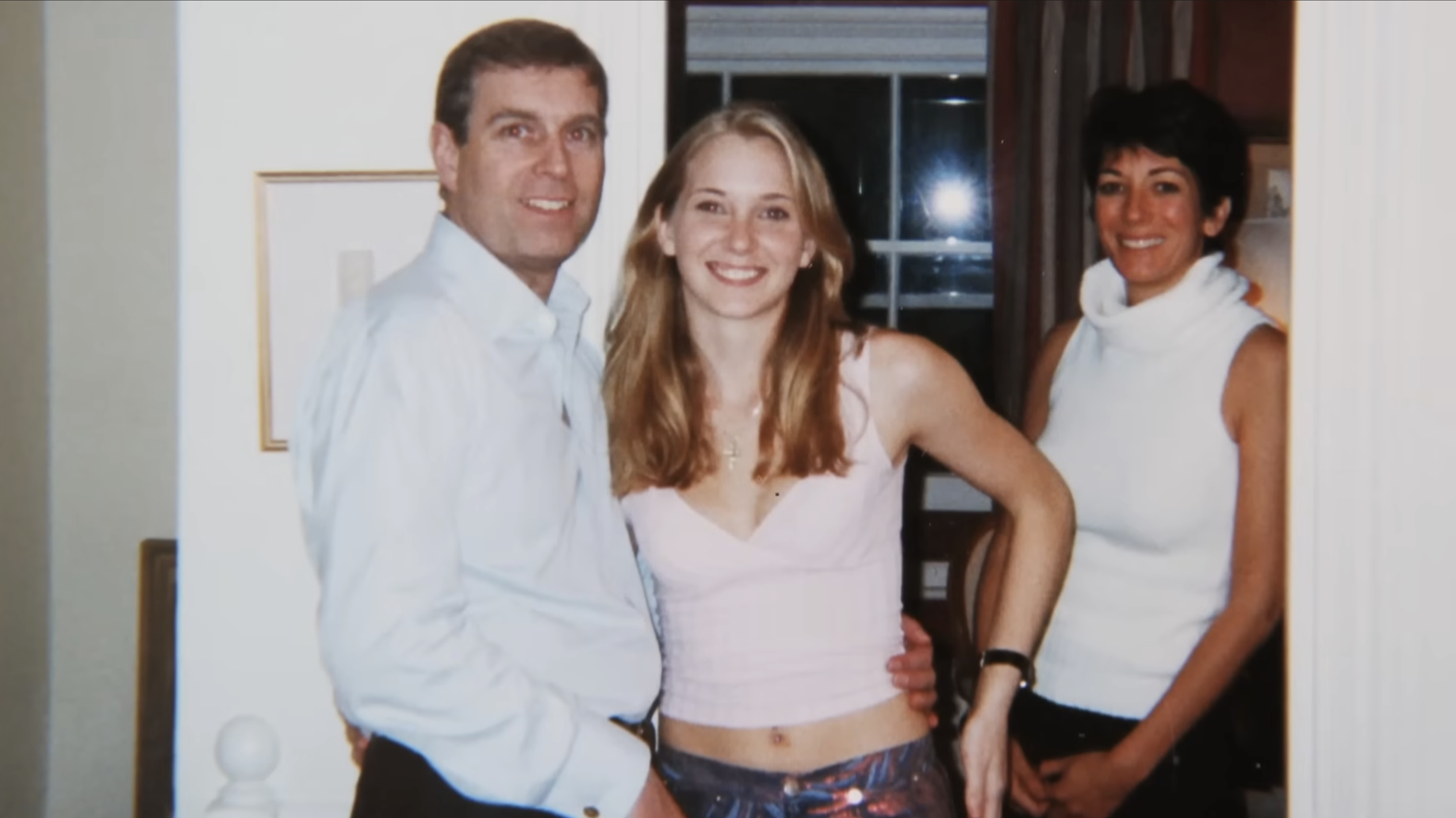 Three smiling people posing together indoors, one man and two women, dressed casually.