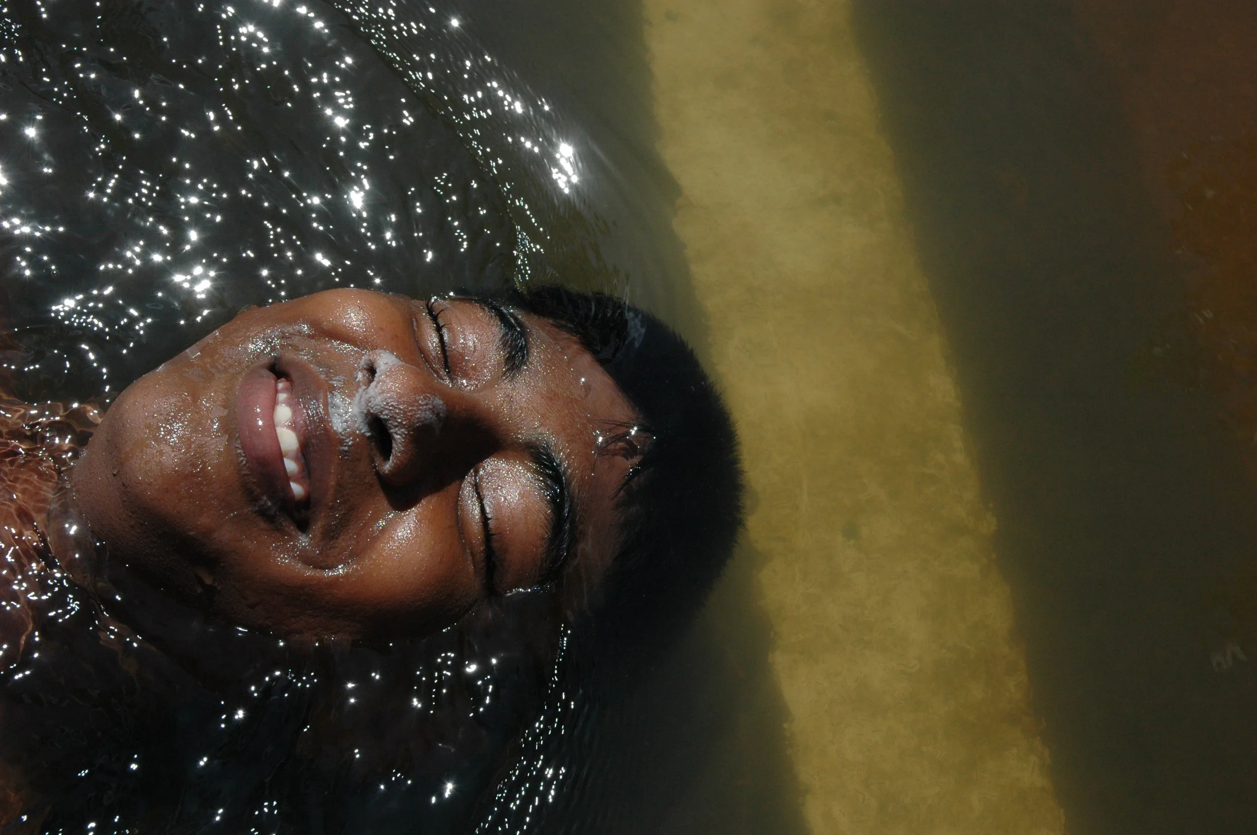 A person with glasses smiling as they float face down in water.
