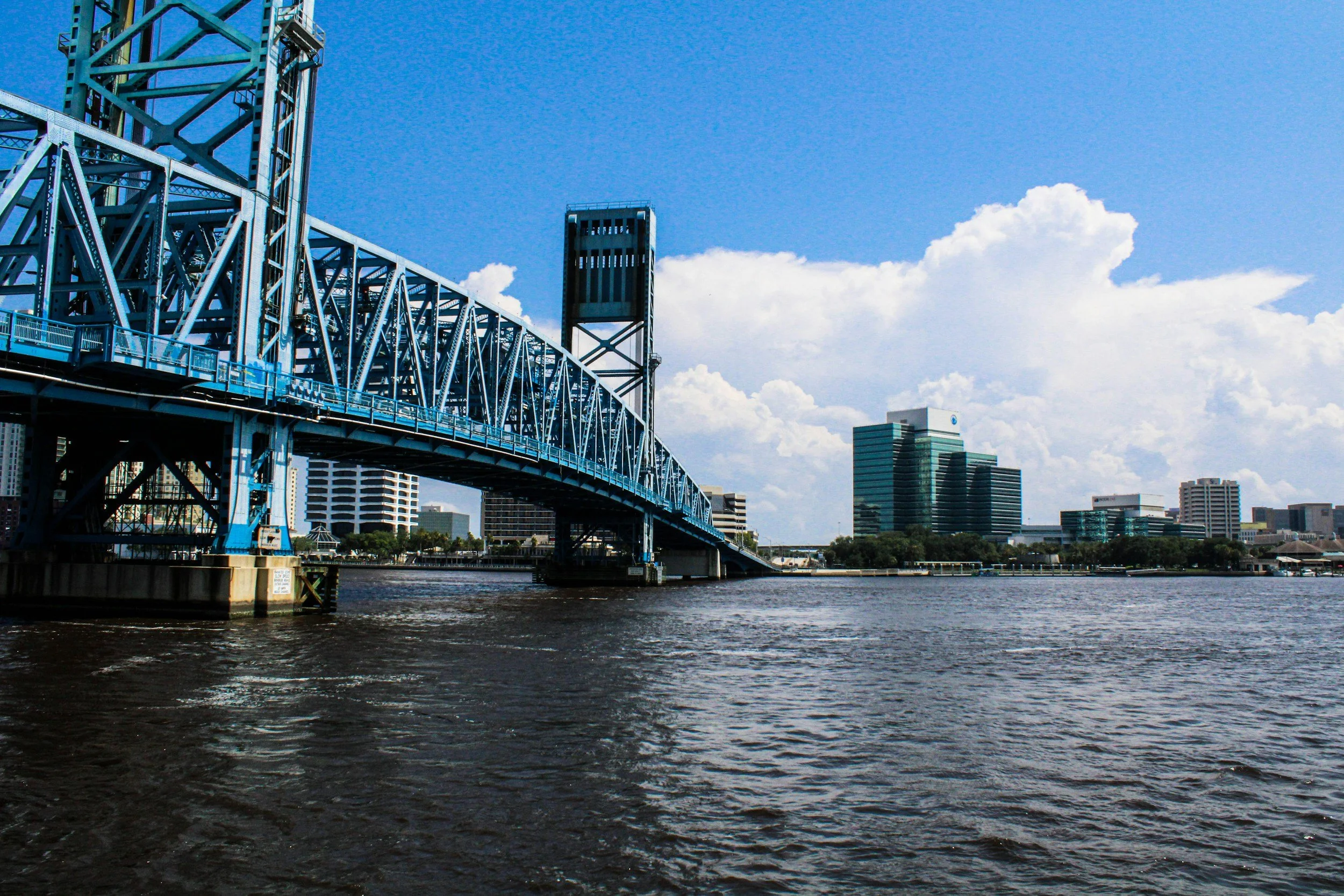 view of main street bridge from jacksonville's southbank in the middle of the day, clear skies wit ha few clouds at the horizon and downtown jacksonville in the background