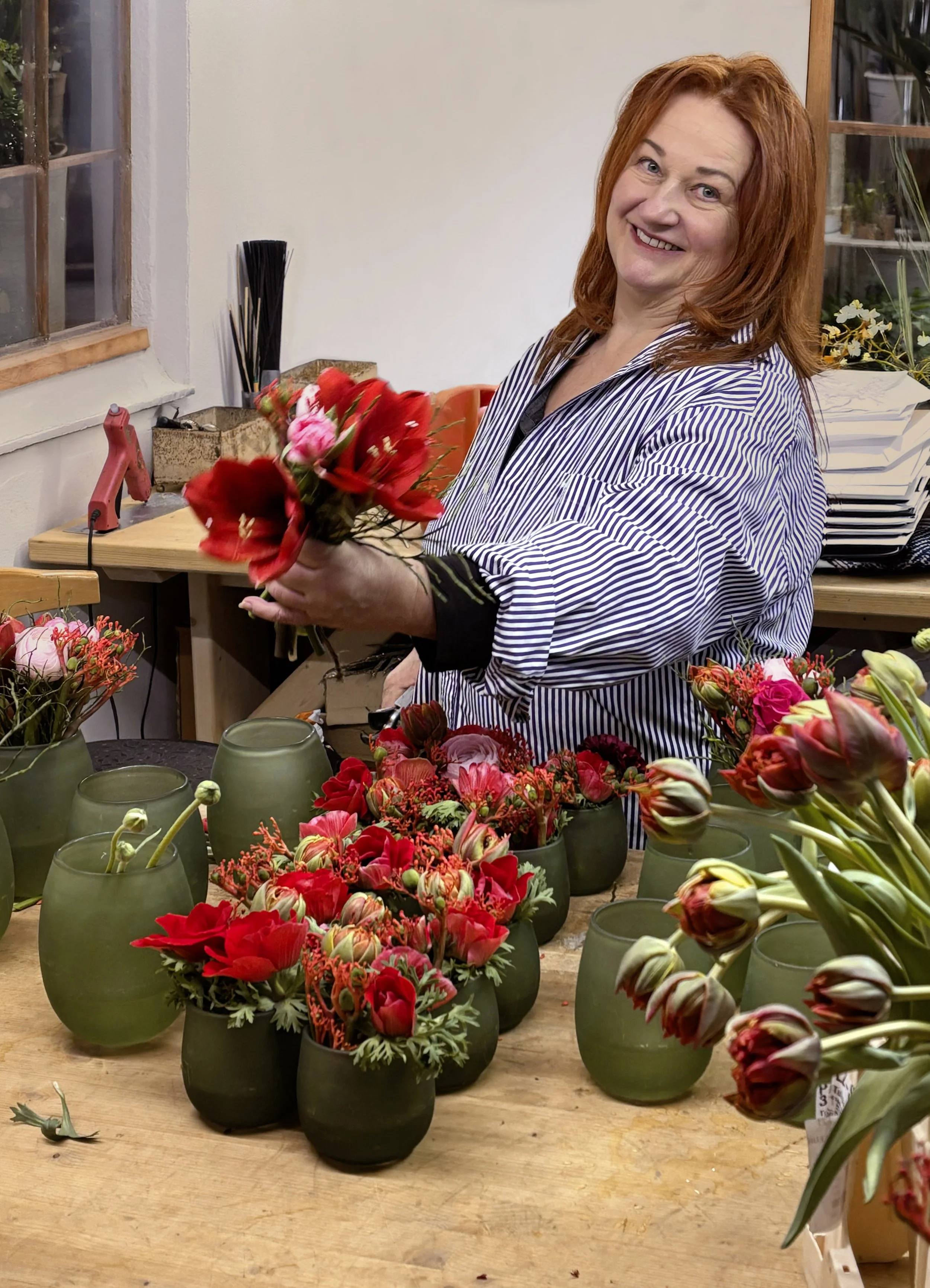 Porträtfoto von Elisabeth Springer in ihrer Werkstatt, beim Arrangieren von Blumensträußen mit roten Blumen in grünen Vasen.