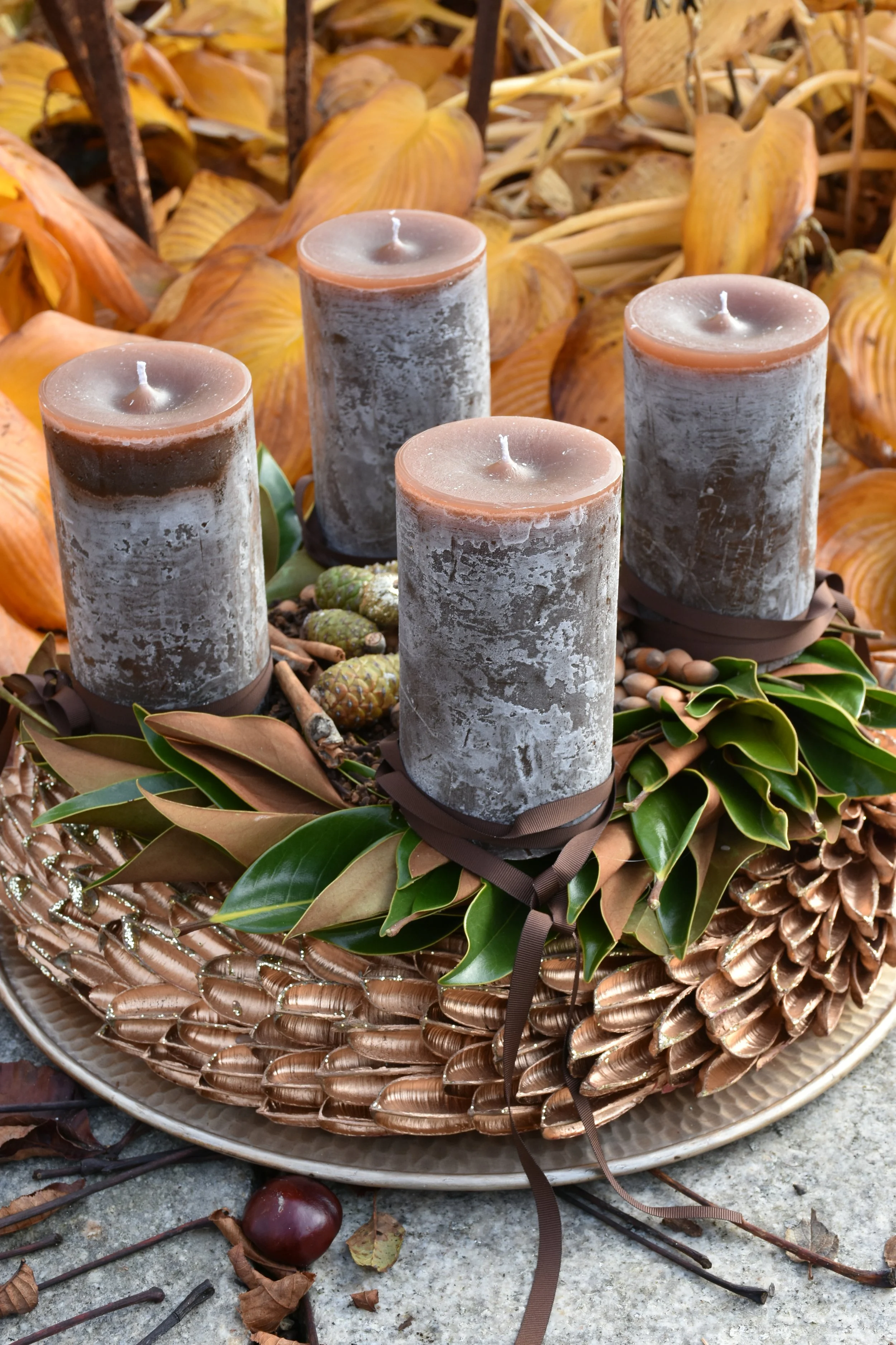 Adventkranz mit grauen Kerzen, Blättern und getrockneten Früchten, mit herbstlichen Dekorationen im Hintergrund.