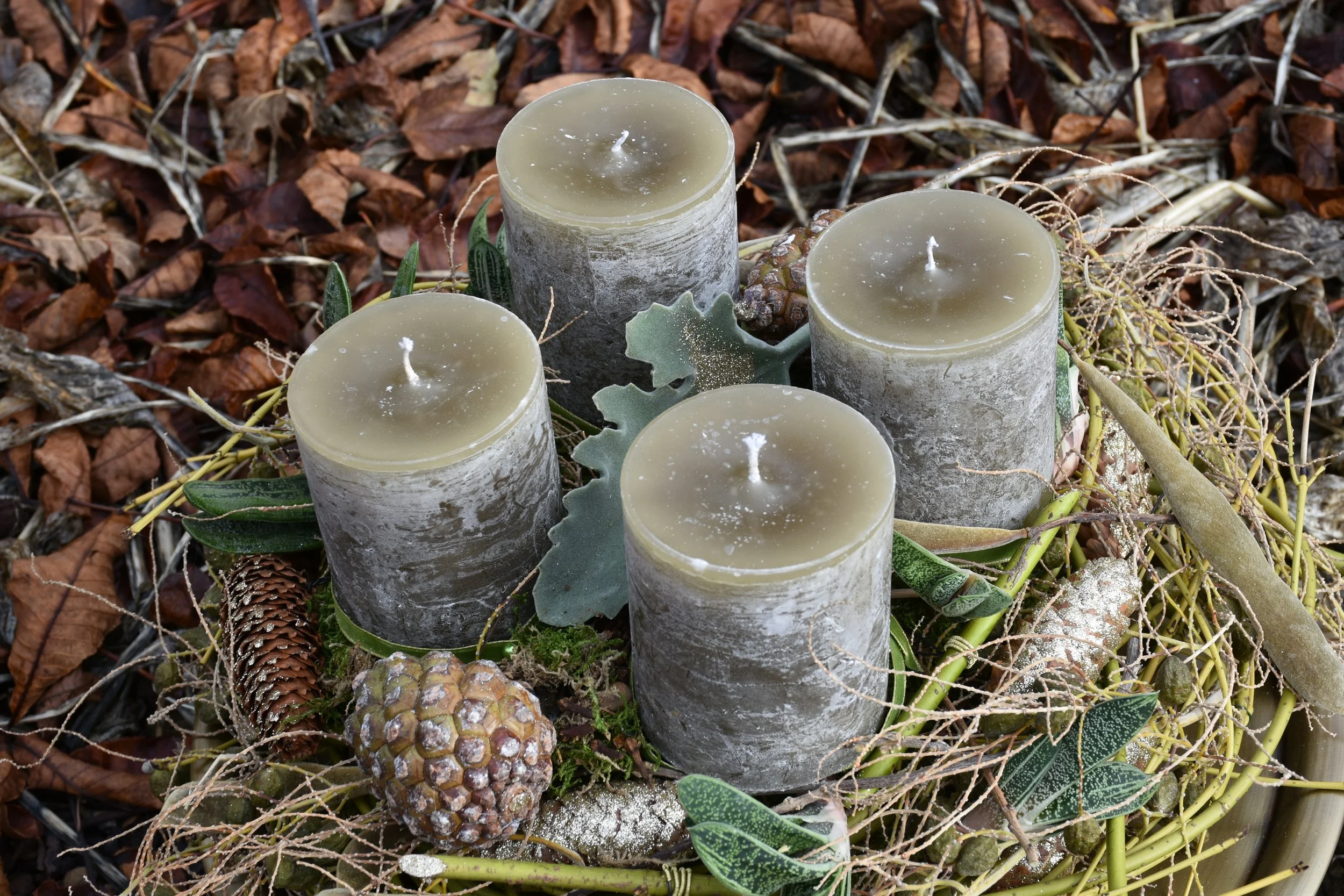 Adventkranz mit grauen Kerzen, mit Tannenzapfen und grünen Blättern.