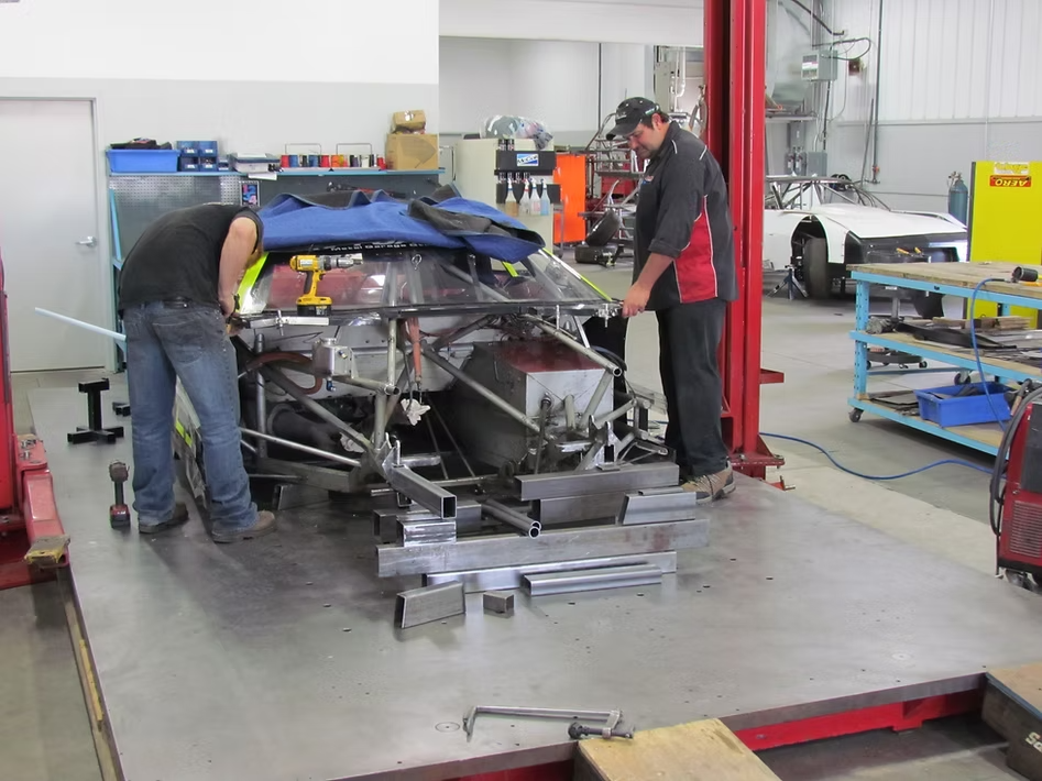 Two automotive technicians working on a race car chassis in a professional workshop