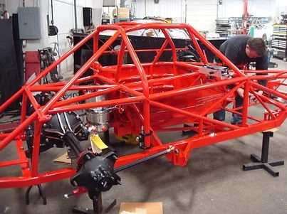 Bright red tubular race car chassis under construction in an automotive workshop