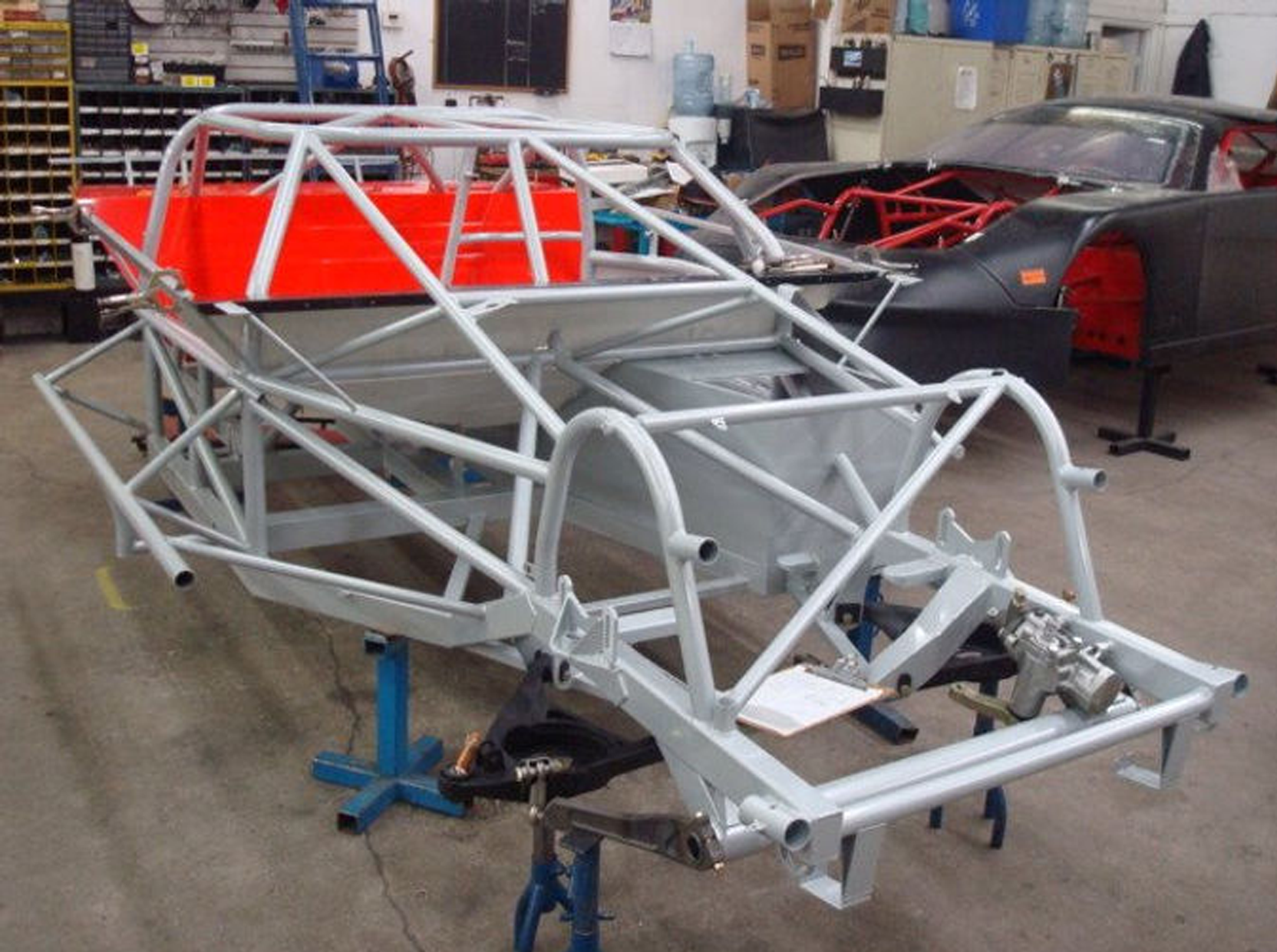 Partially assembled off-road buggy chassis with white roll cage in an automotive workshop