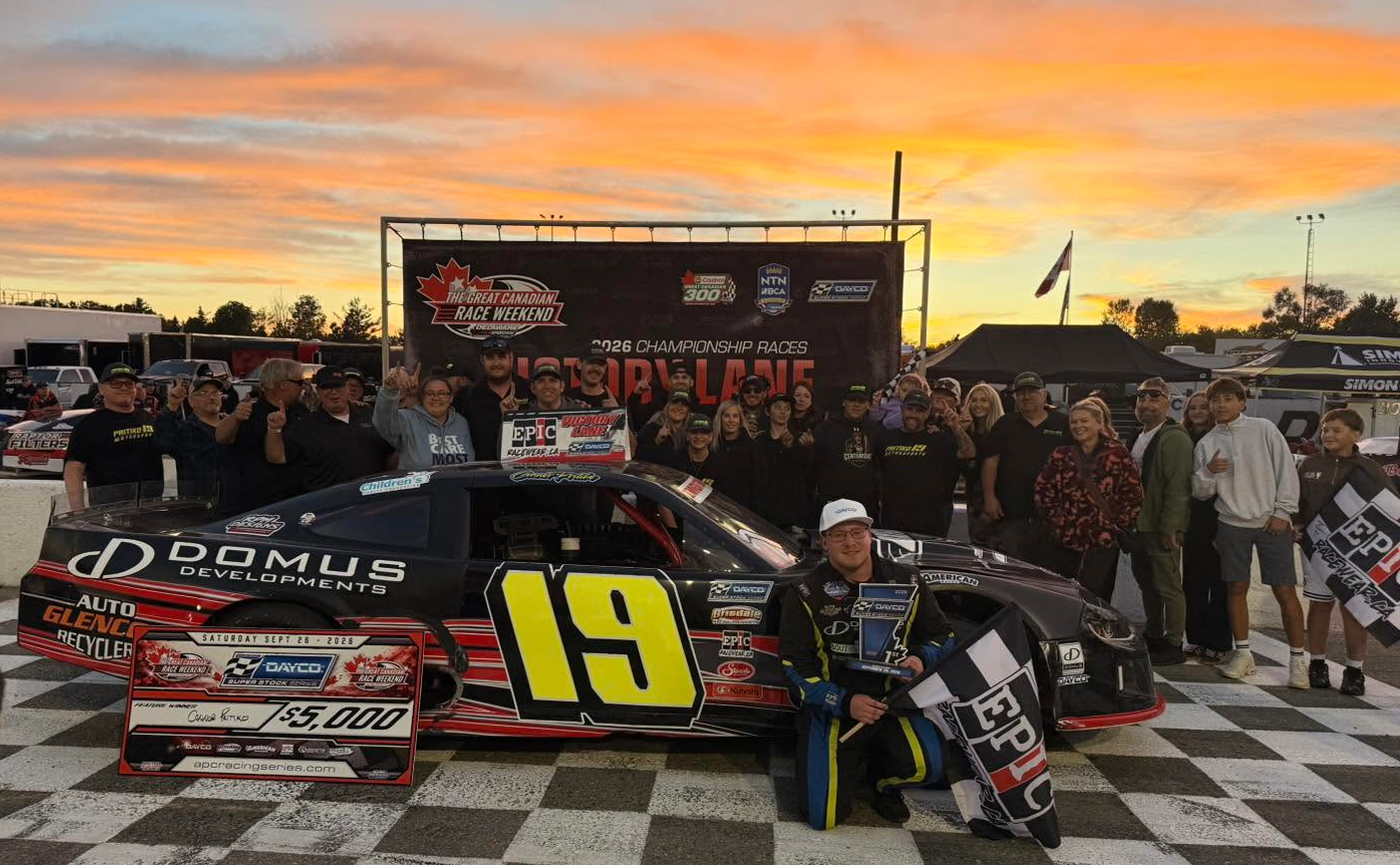 Race team and supporters pose with a black No. 19 stock car, trophy, and oversized $5,000 check at the Great Canadian Race Weekend.