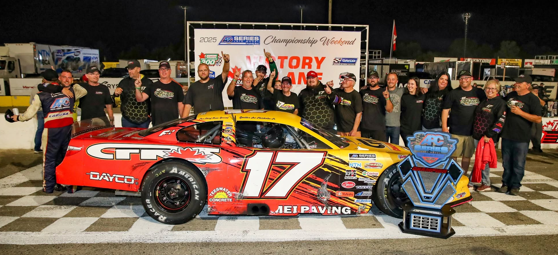 Race team celebrating beside a red-and-yellow No. 17 stock car and championship trophy at the 2025 APC Series Championship Weekend