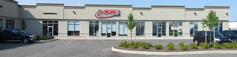 Exterior of a commercial shopping center with an M&R dealership storefront, parked cars, and landscaped parking lot.