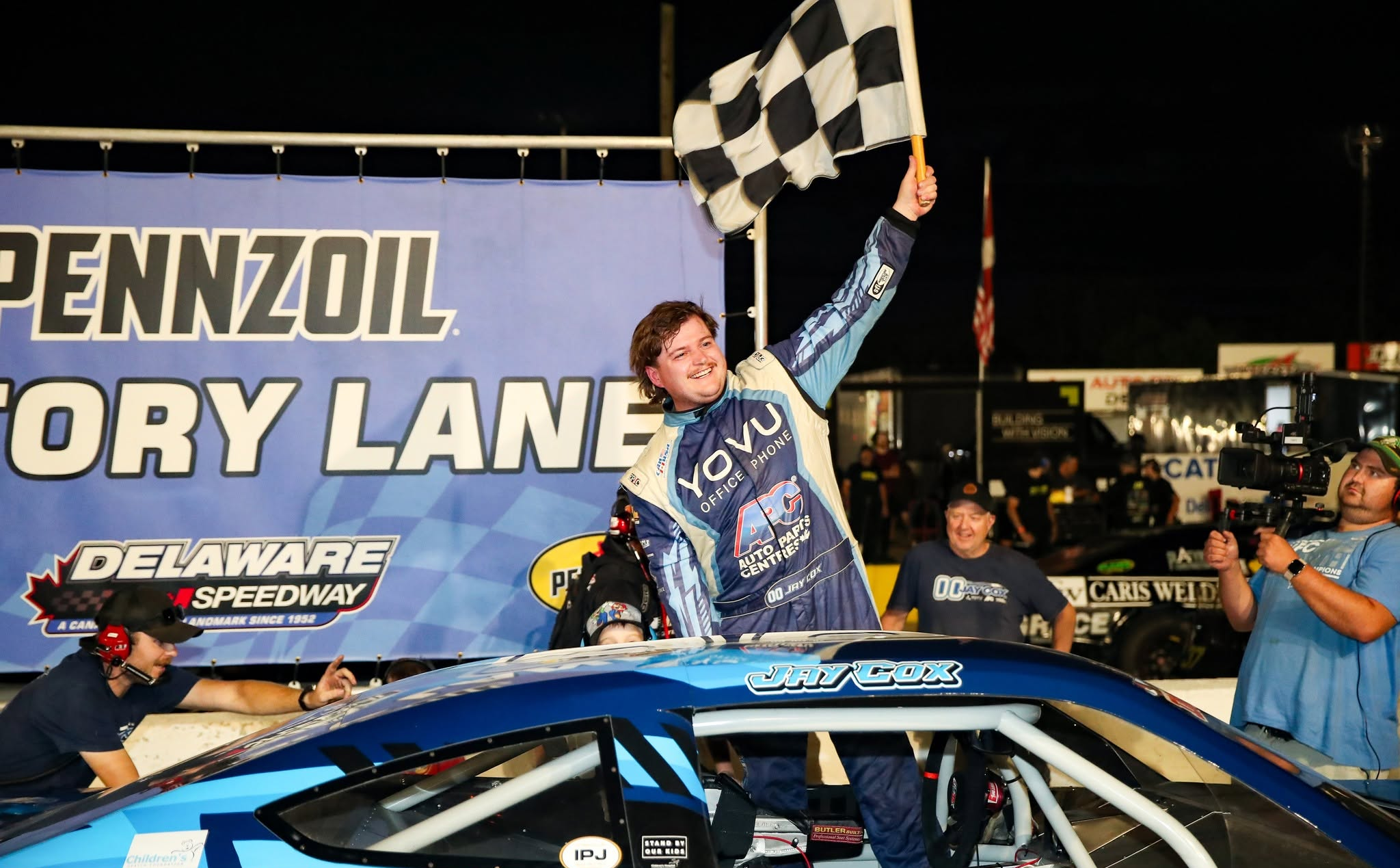 Race car driver Jay Cox celebrates atop his car while waving a checkered flag at Delaware Speedway.