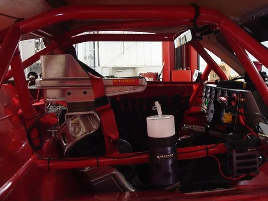 Interior of a red off-road racing vehicle with roll cage, racing seats, dashboard controls, and a water bottle