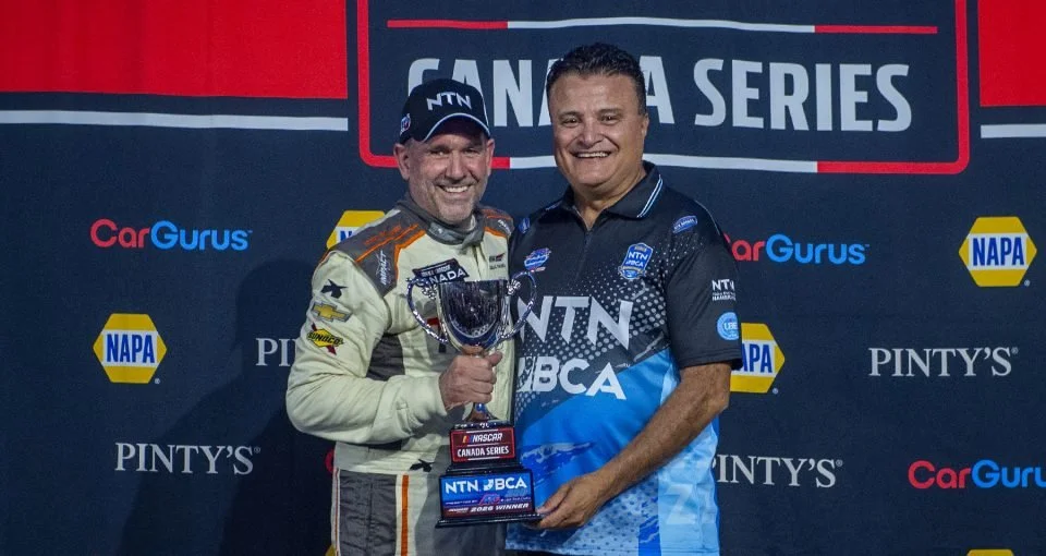 Donald Theetge NASCAR Canada Series driver holding a trophy beside an NTN BCA team representative at a sponsor podium