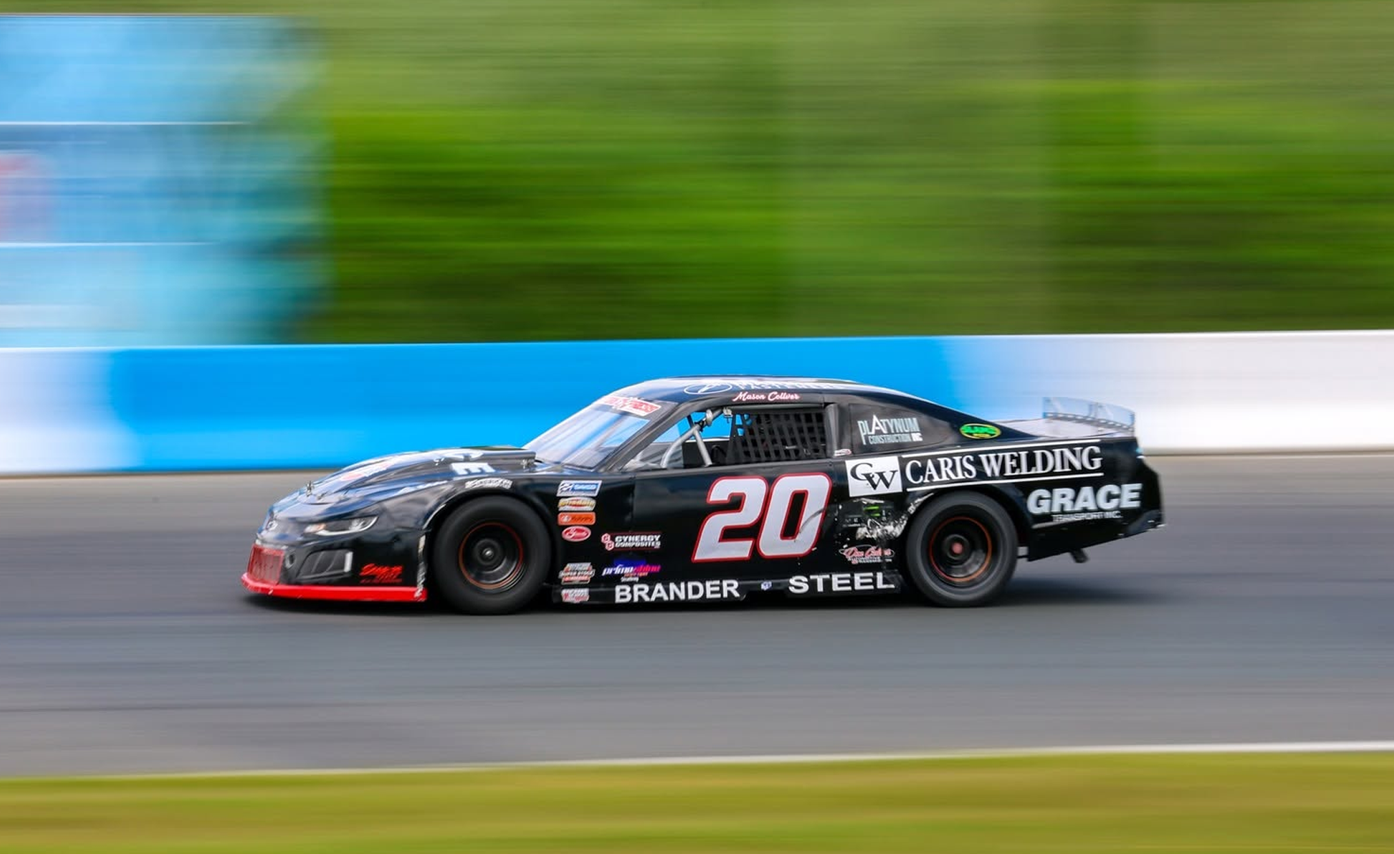 Black No. 20 stock car racing around a track with motion-blurred green scenery