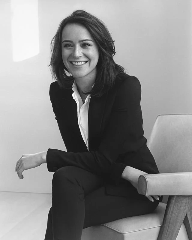Black-and-white portrait of a smiling businesswoman in a blazer seated in a modern armchair
