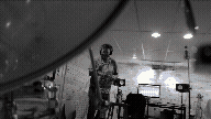 A person standing in a room with sound equipment, including microphones and speakers, possibly a recording studio.