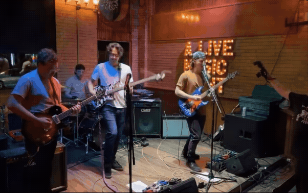 A band performing live music on stage in a cozy indoor venue with decorative wall signs.