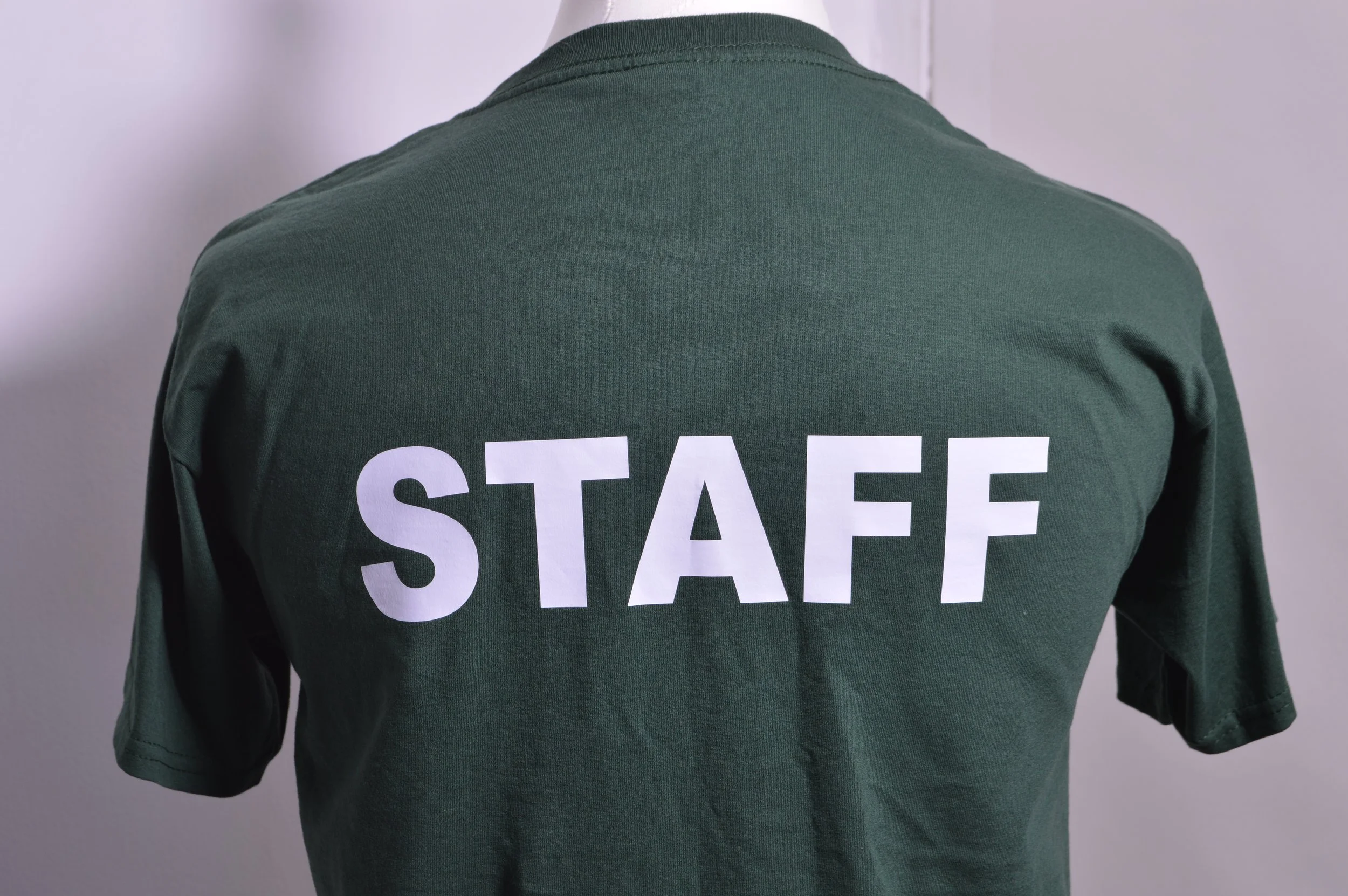 Back of a person wearing a green shirt with the word 'STAFF' printed in large white letters on the back.