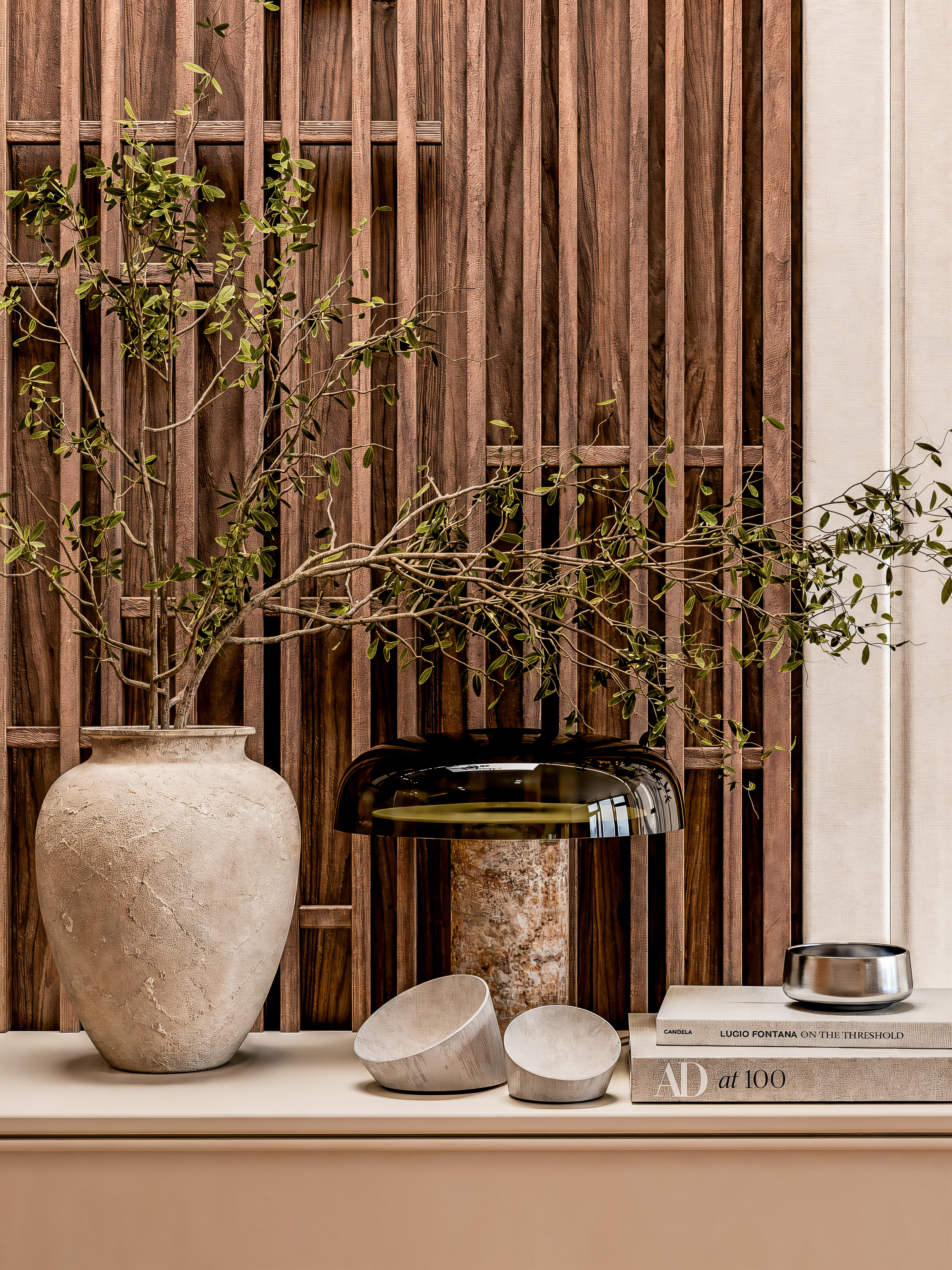 Decoração com vasos de cerâmica em vários tamanhos e cores neutras, um lustre de vidro dourado, um livro de design, uma tigela de metal prateada e uma parede de painel de madeira com acabamento escuro.