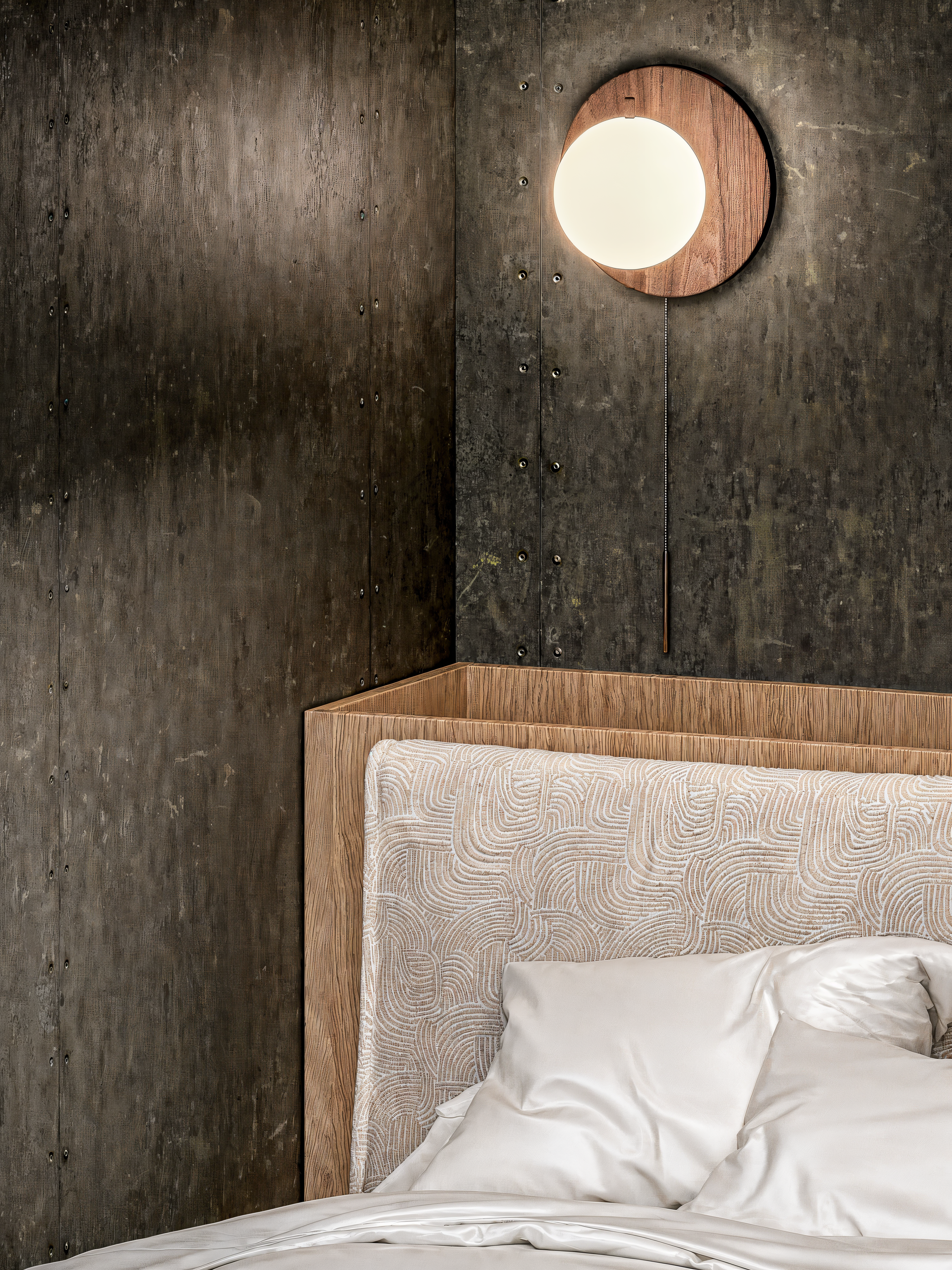 Cabeceira de cama de madeira com tecido texturizado, cama com roupa branca, parede de concreto escuro com superfície texturizada e uma luminária circular de madeira na parede.