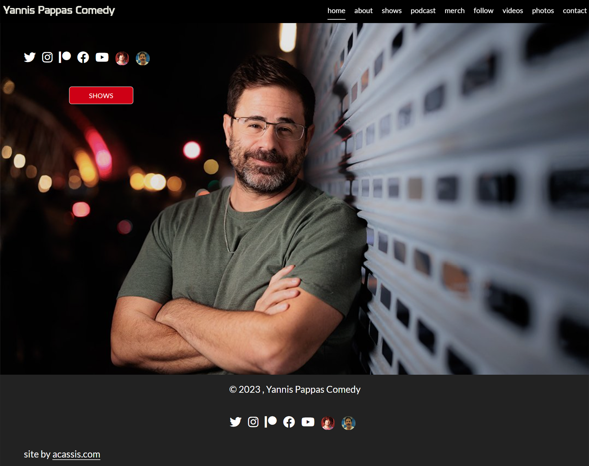 Website homepage for Yannis Pappas Comedy featuring a man with glasses and a beard, standing with arms crossed against a metallic wall at night with blurred city lights in the background. The site has social media icons, a red 'Shows' button, and navigation menu at the top.