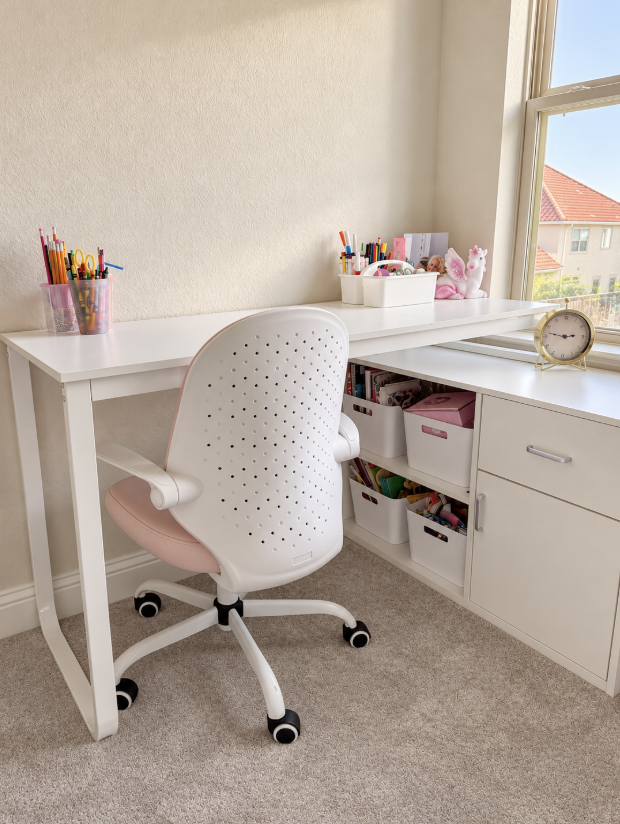 Organized children's bedroom workspace featuring a white desk, pink desk chair, and neatly arranged school and art supplies.