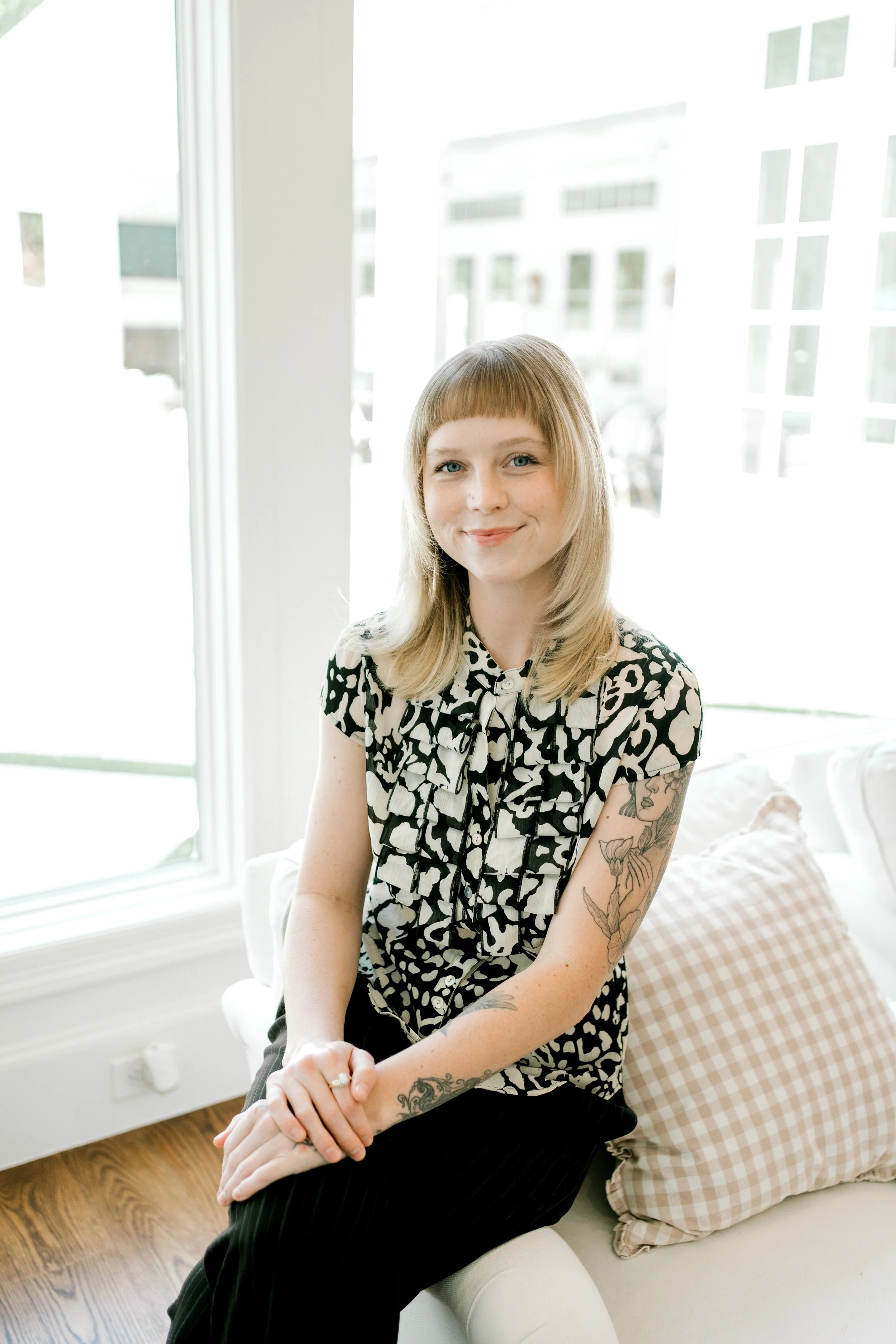 Chloe, professional home organizer at OrganizePro, seated beside a bright window wearing a black-and-white patterned blouse