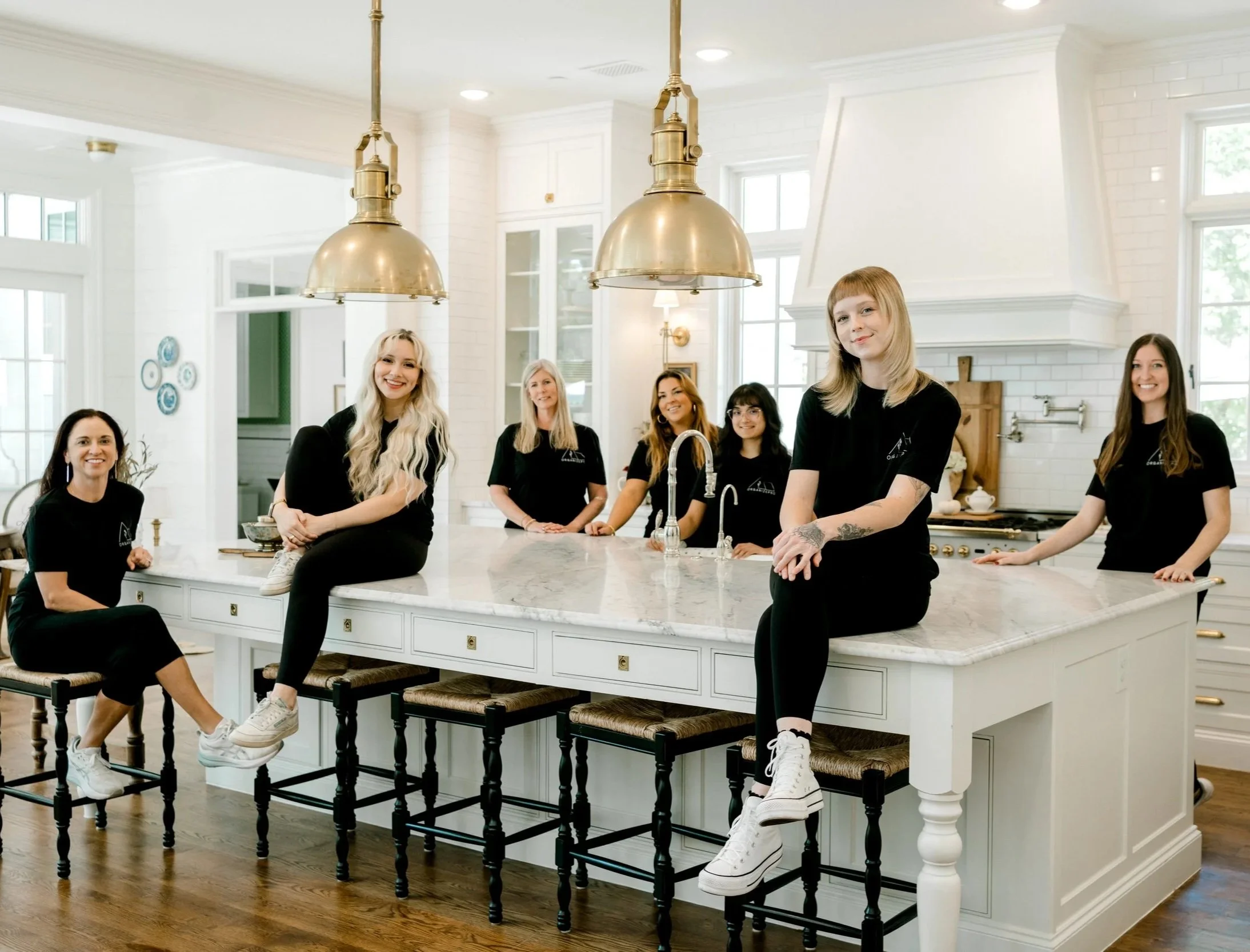 Seven OrganizePro professional home organizers posing together in a bright, beautifully designed kitchen in Frisco, TX.