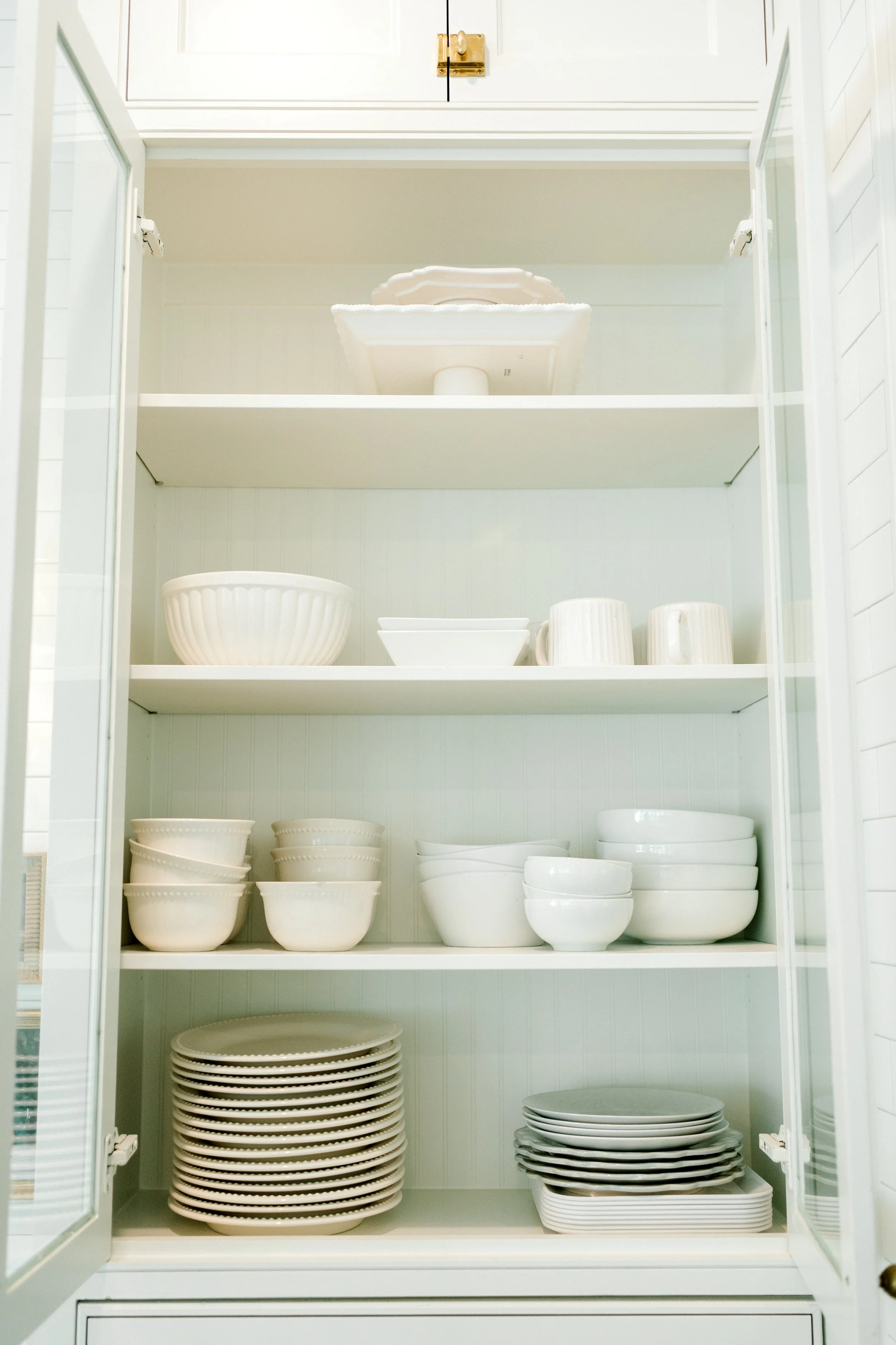 Open white kitchen cabinet with neatly arranged plates, bowls, and serving dishes organized on shelves for easy access.