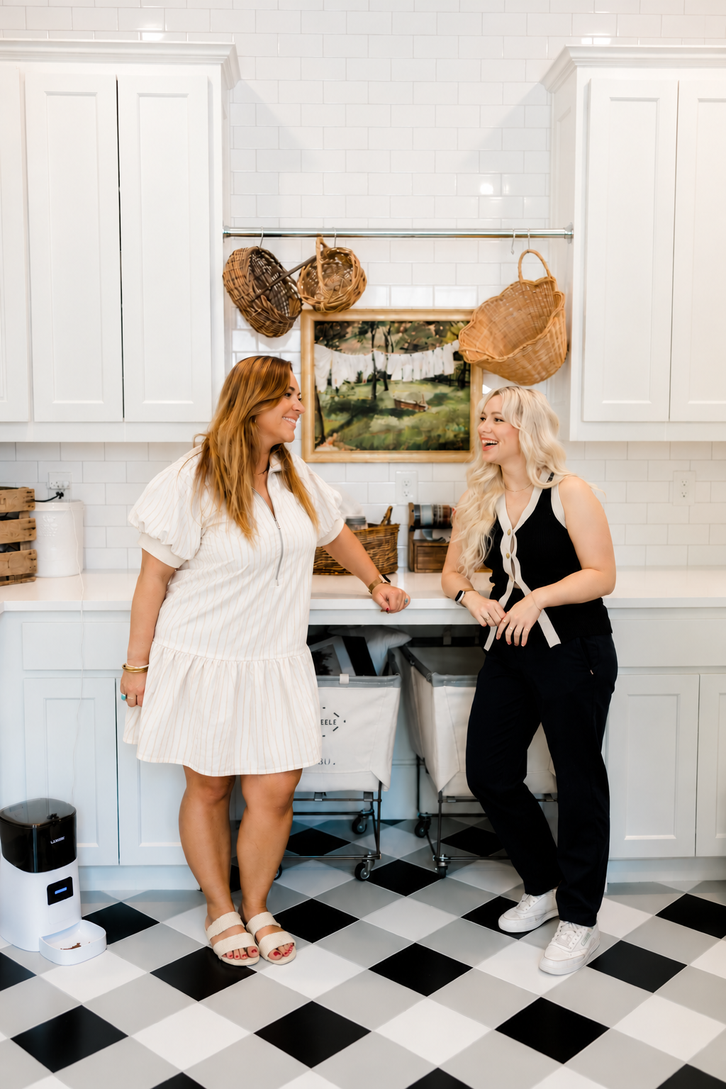 Two OrganizePro team members smiling and talking in a bright, organized laundry room reflecting the company's friendly, judgment-free approach to professional home organizing.
