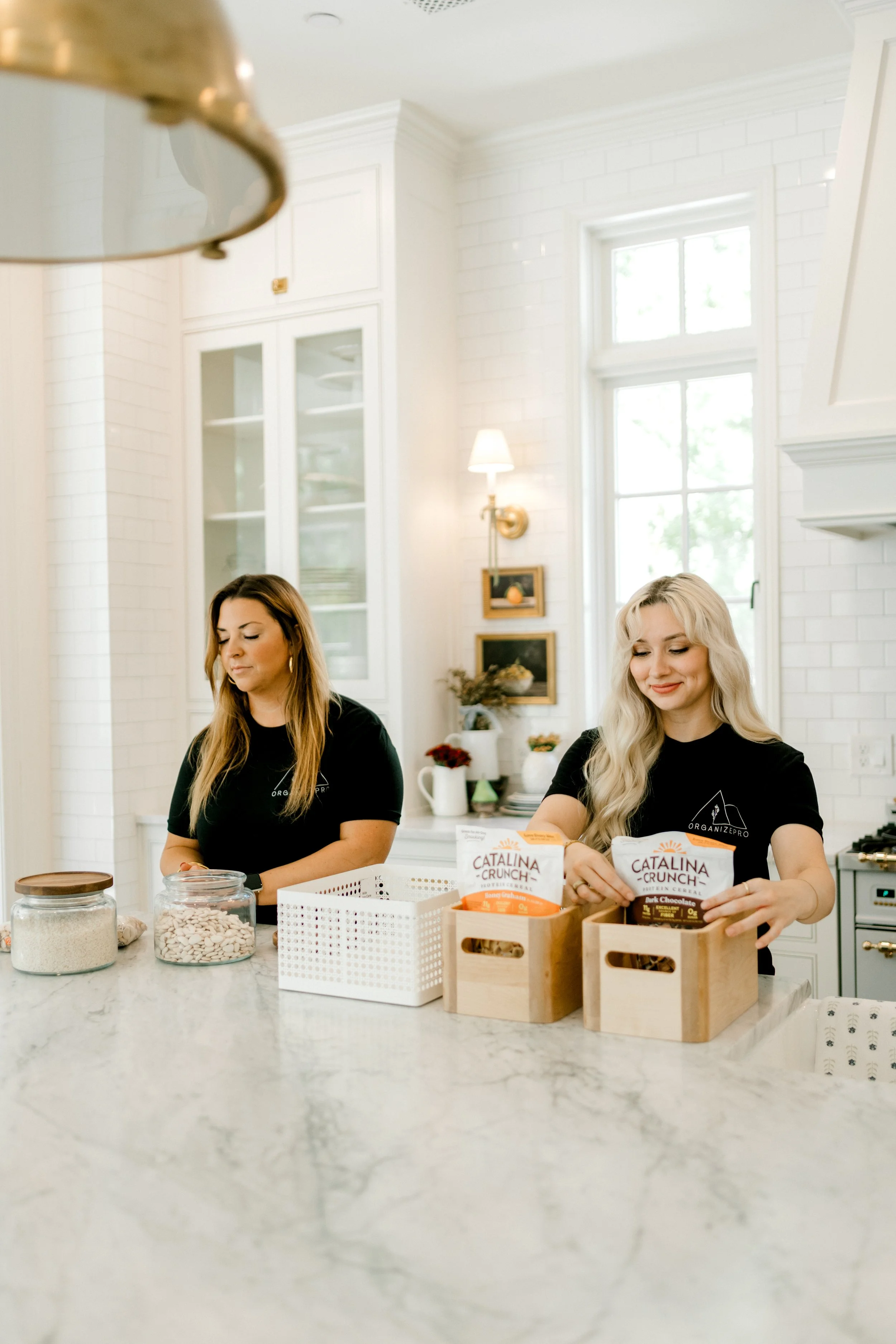 Two OrganizePro team members organizing pantry essentials and creating functional storage systems in a beautifully designed kitchen.