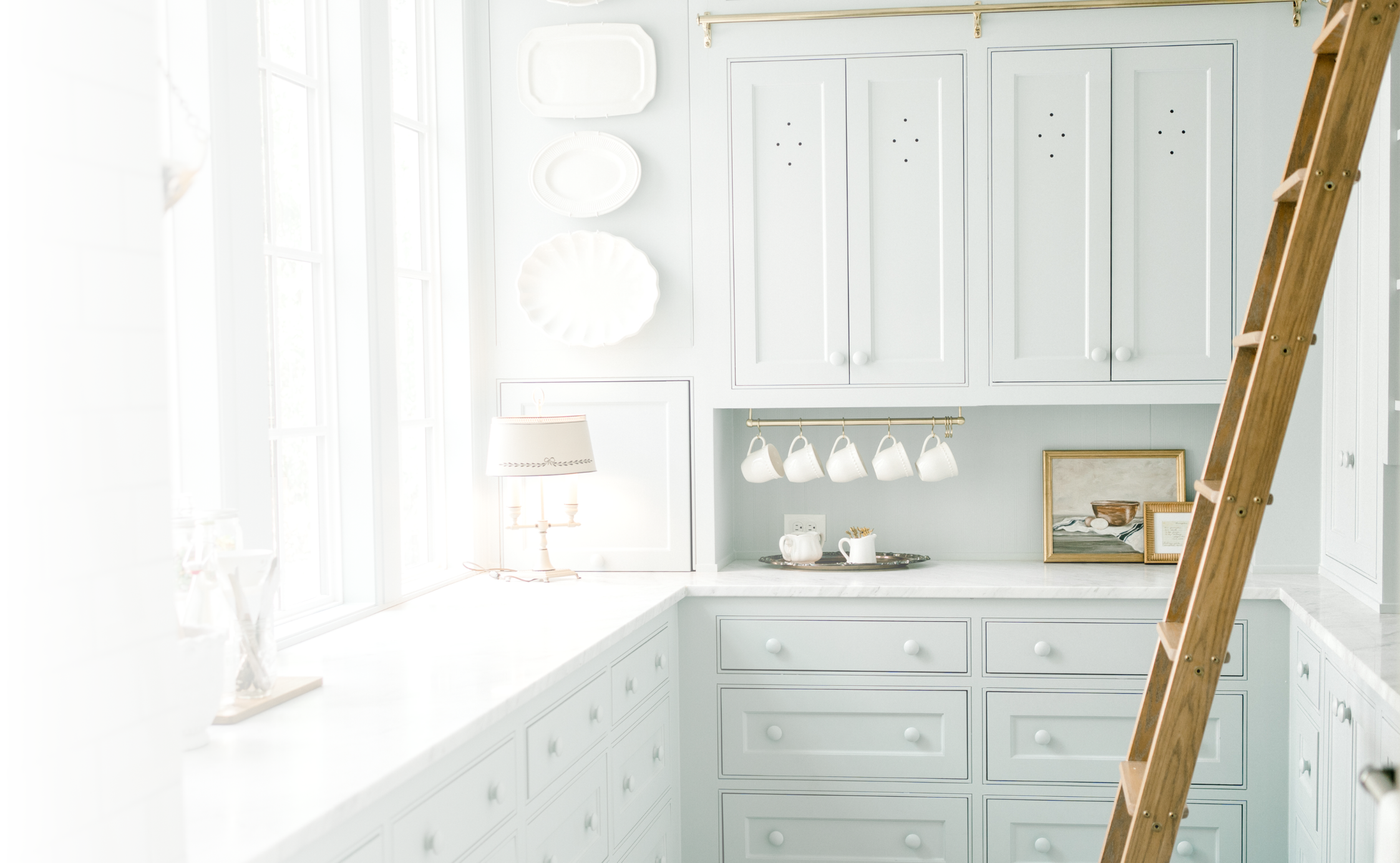 Beautifully organized light blue kitchen with custom cabinetry, open shelving, and a wooden ladder, showcasing OrganizePro’s luxury home organizing services in Frisco, TX