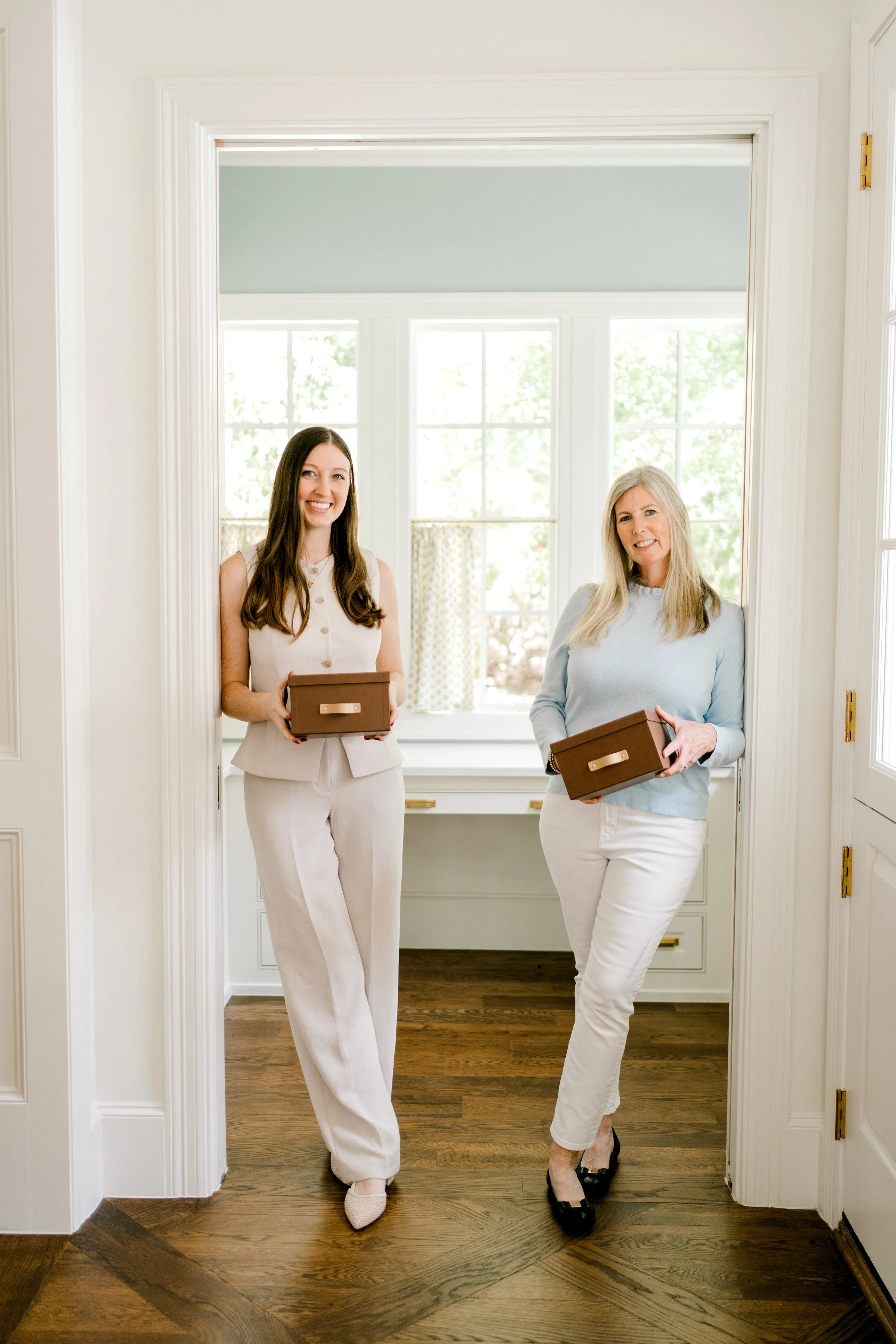 Two OrganizePro professional home organizers holding storage boxes in a bright, beautifully organized home office.
