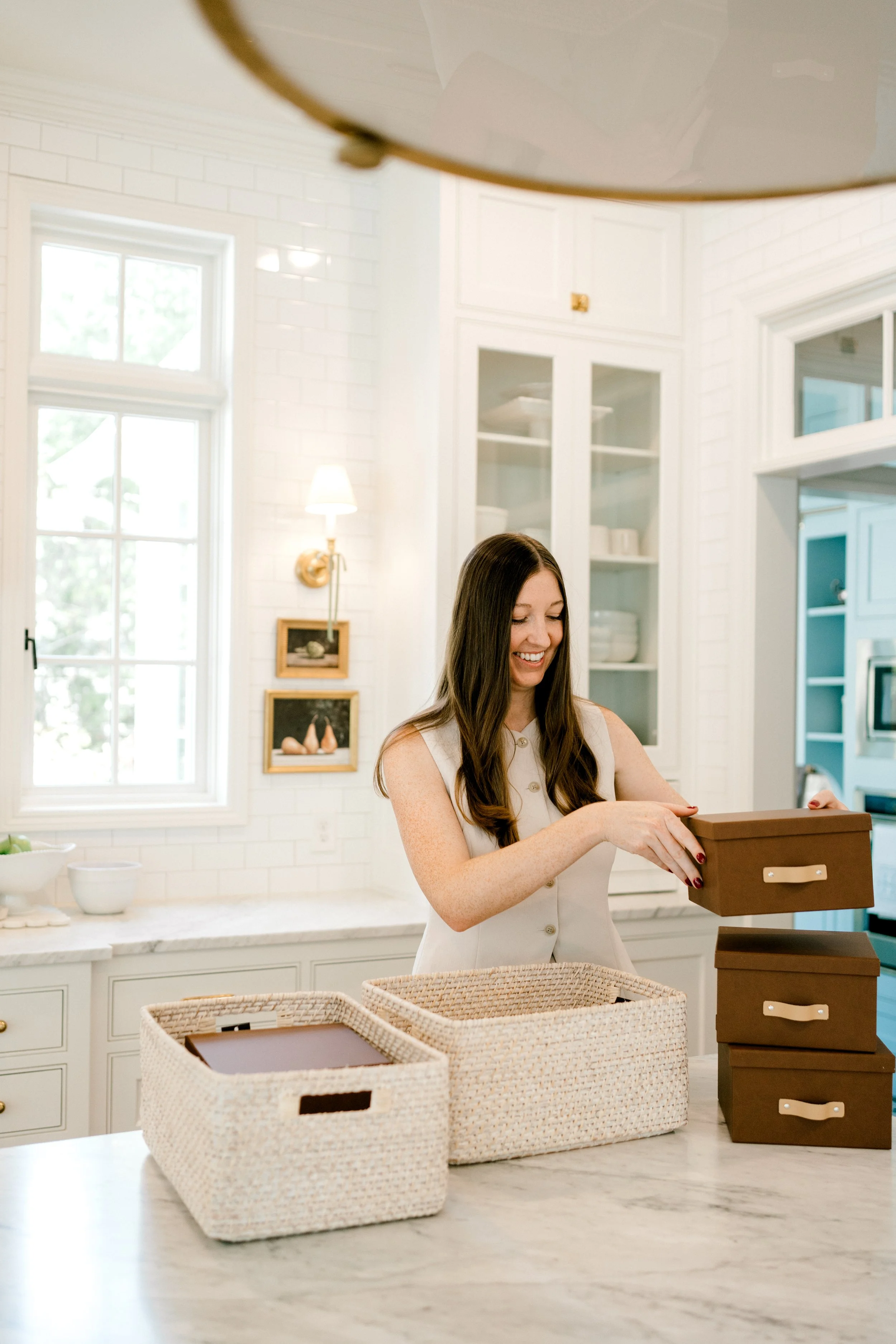 OrganizePro founder arranging decorative storage boxes and woven baskets on a kitchen island to create functional household organization systems.