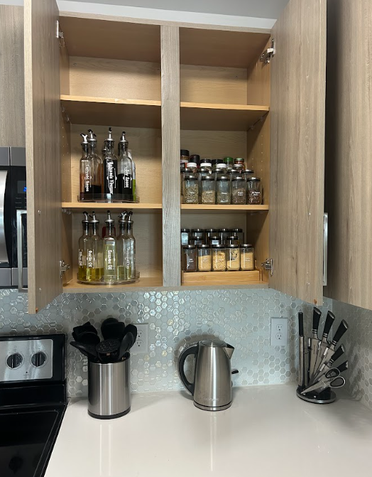 Organized wooden kitchen cabinets featuring neatly arranged spices, cooking oils, and seasonings in functional storage systems.