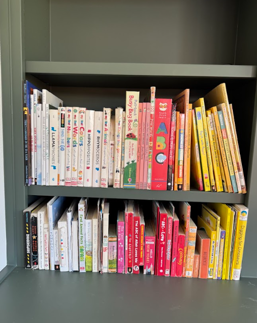 Children's books neatly arranged by color on dark green built-in bookshelves, creating an easy-to-maintain organization system.