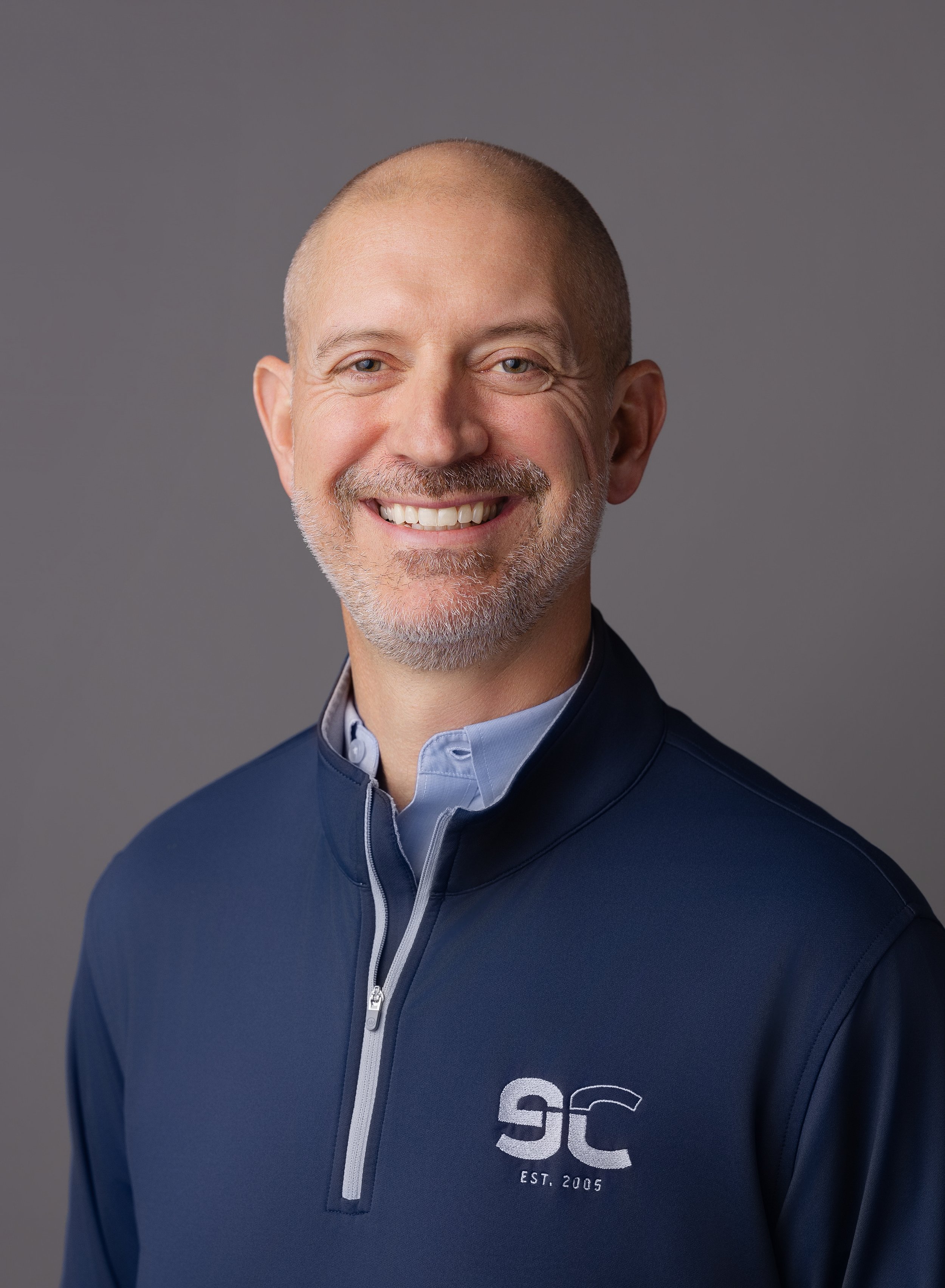 Josh Simmons, wearing a navy blue pullover with a quarter-zip collar, white zipper, and an embroidered eCatholic logo on the chest.