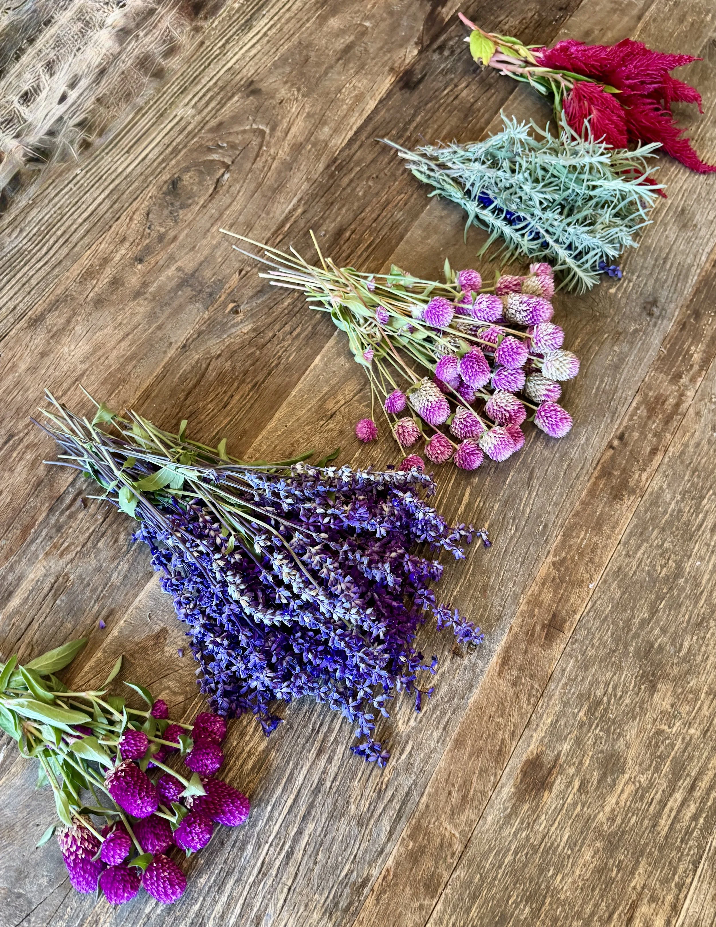 Several bouquets of flowers in different colors, including purple, pink, blue, and red, laid out on a wooden surface.