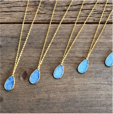 Five gold necklaces with blue teardrop-shaped pendants laid on a wooden surface.
