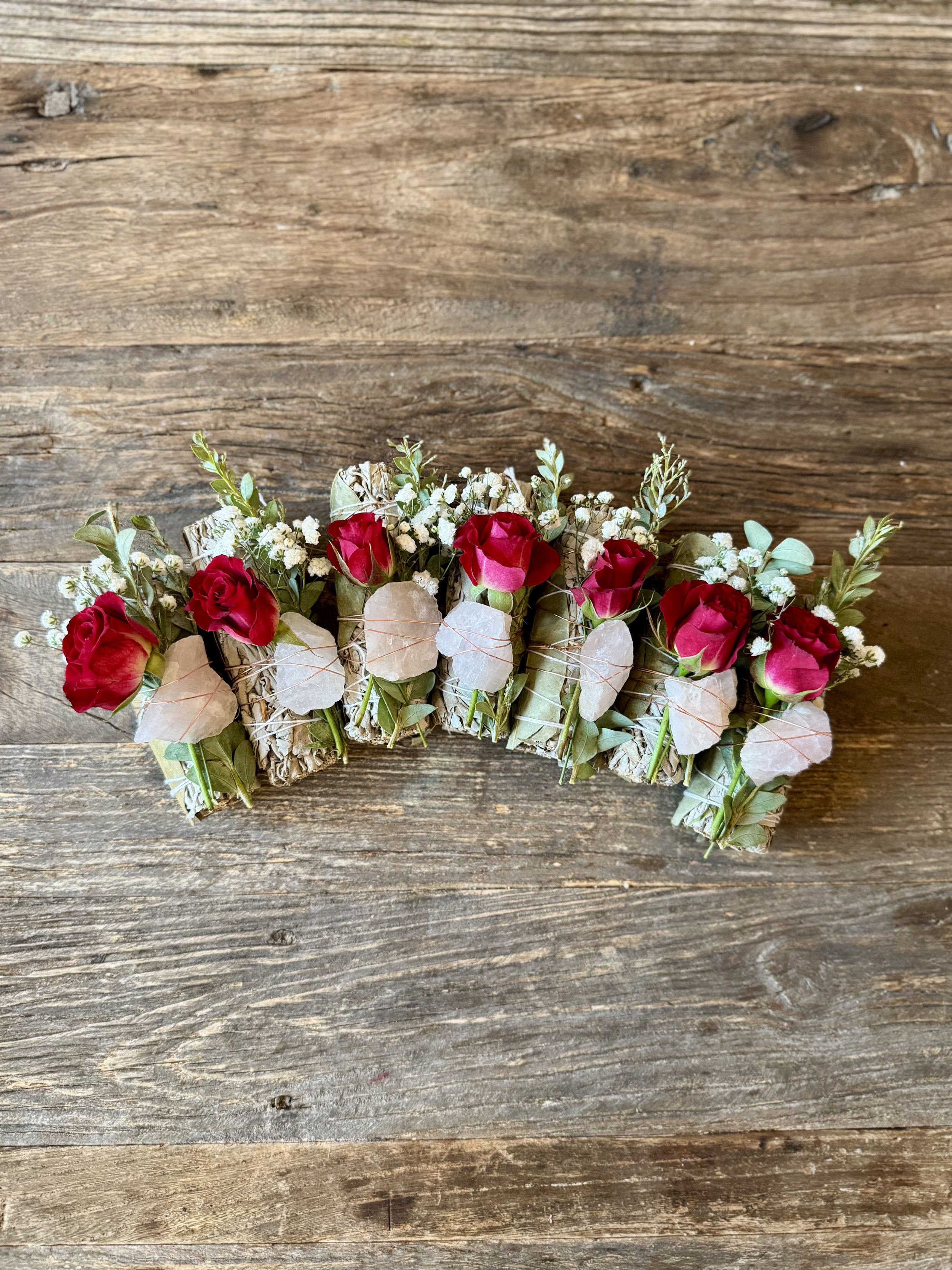 A floral arrangement featuring red roses, white baby's breath, and green foliage in a rustic container, placed on a weathered wooden surface.