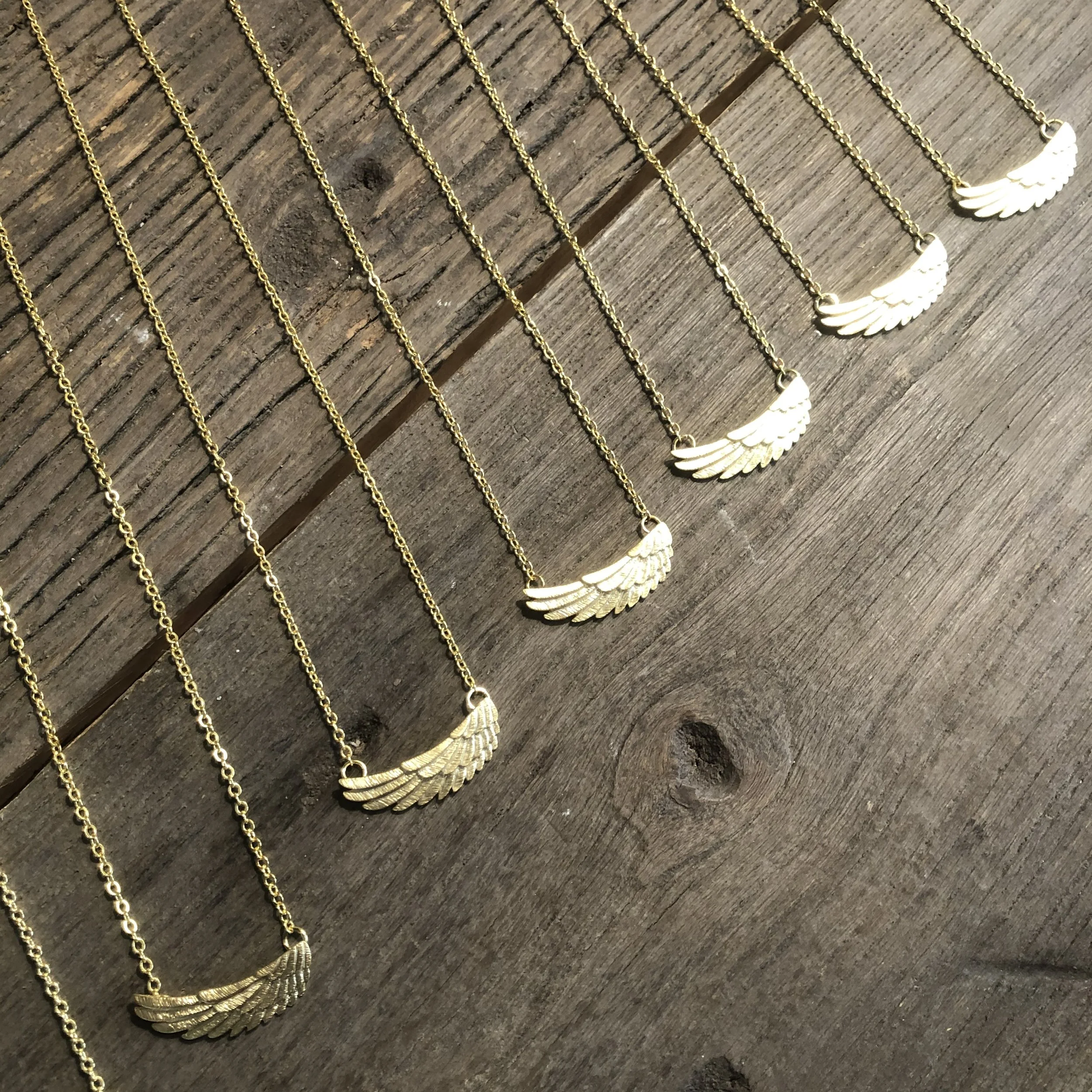 Several gold necklaces with wing-shaped pendants arranged on a rustic wooden surface.
