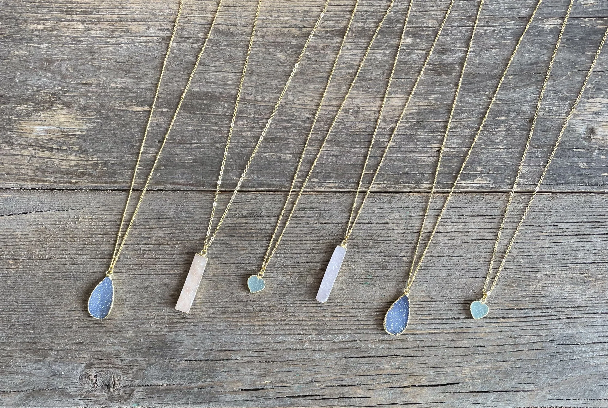 Multiple gold necklaces with rectangular and teardrop pendants on a wooden surface.