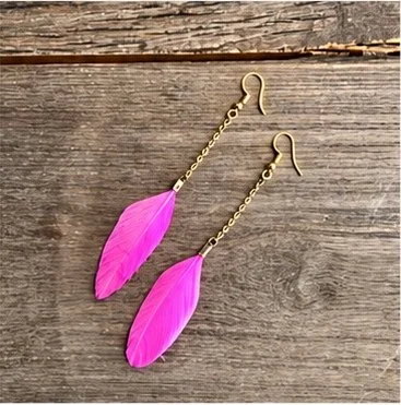 Pink feather earrings with gold hooks on a wooden surface.